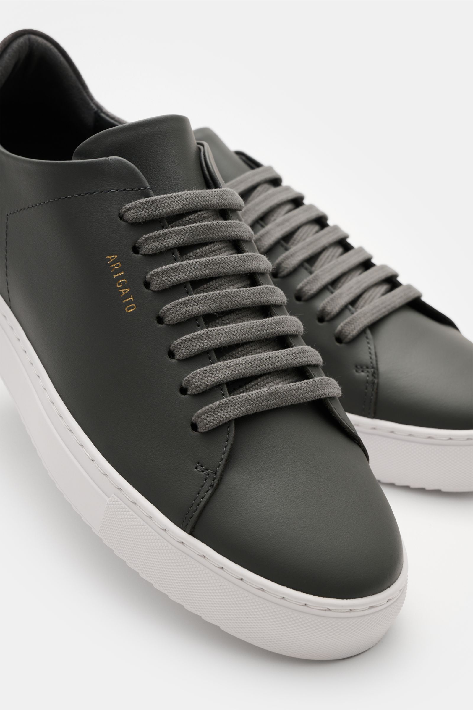 Axel Arigato Sneaker 'Clean 90' dunkelgrau aus edlem Glattleder, runde Vorderkappe, Sieben-Loch-Schnürung, goldfarbene Prägung, flexible Gummisohle, Nahaufnahme schräg von vorne.