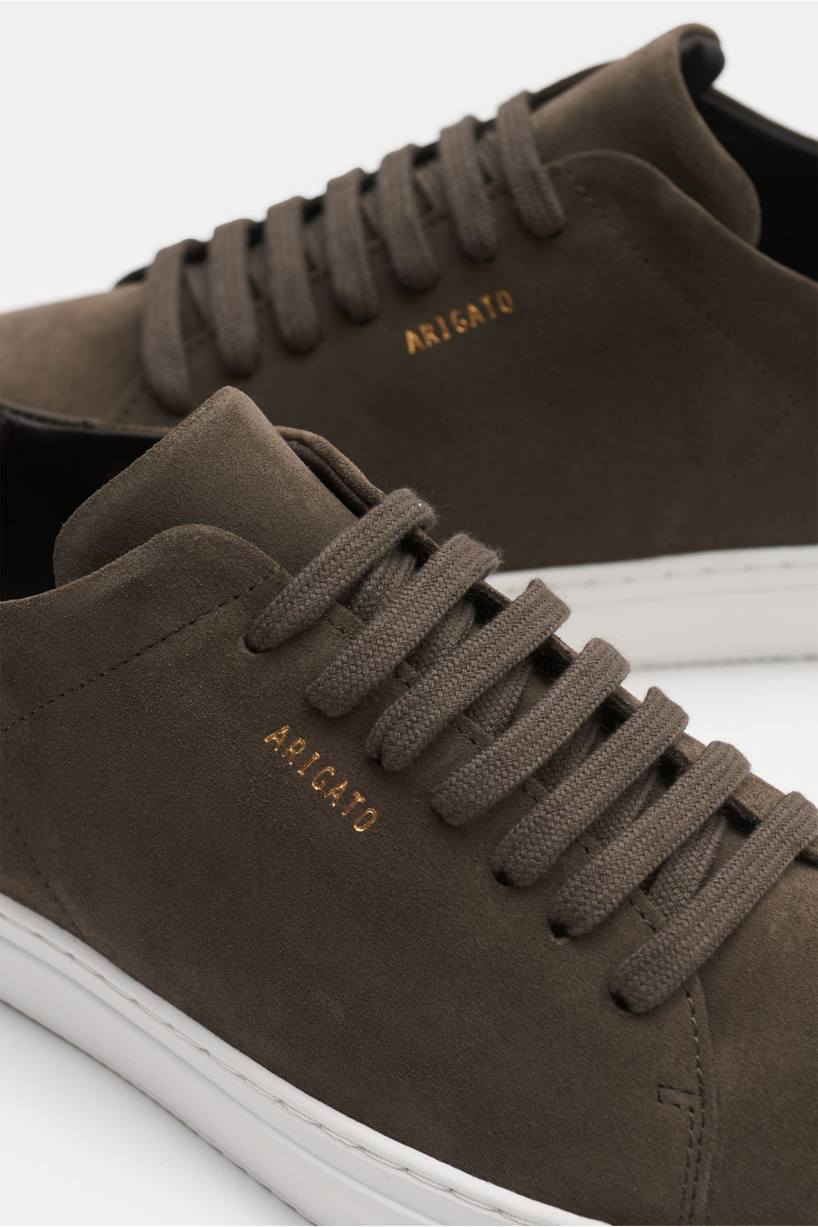 Axel Arigato Sneaker 'Clean 90' graubraun aus edlem Veloursleder, sieben-Loch-Schnürung, goldfarbene Prägung, flexible weiße Sohle, Nahaufnahme seitlich.