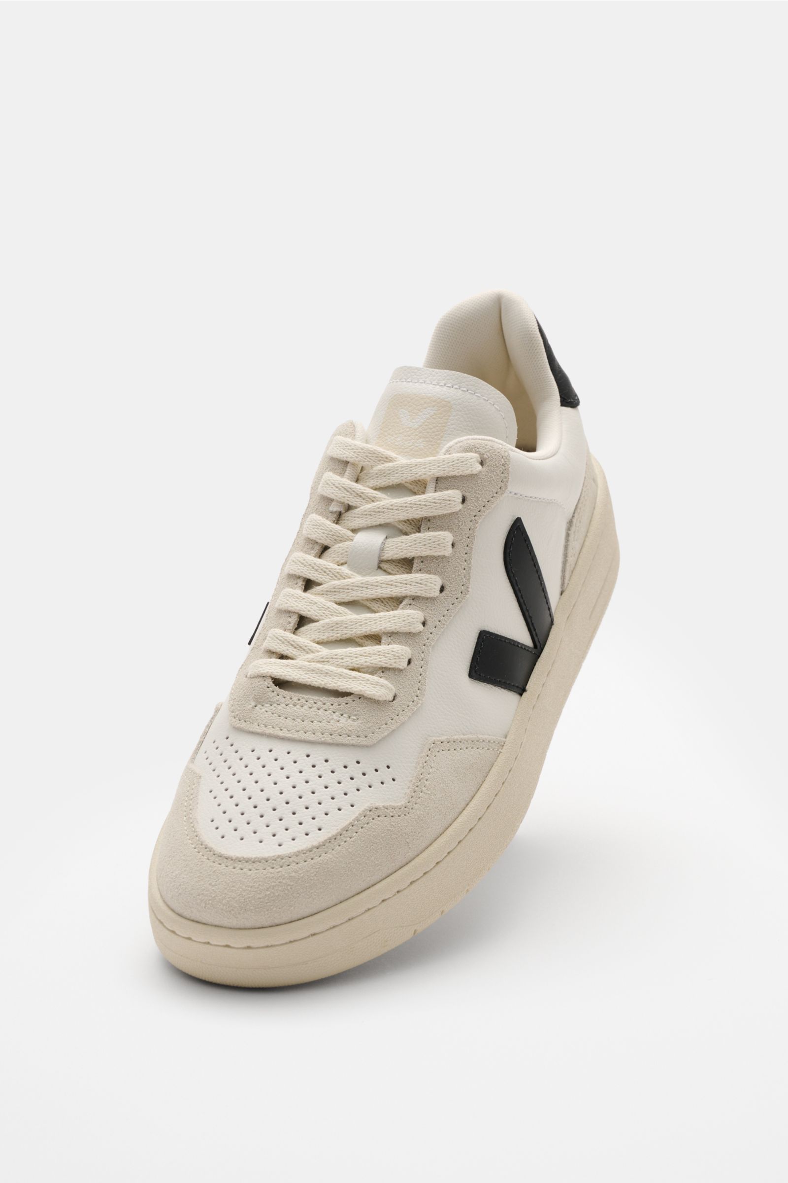 Veja Sneaker 'V-90 O.T. Leather' offwhite/schwarz shown from a front angle, featuring sustainable leather, perforated round toe, seven-hole lacing, padded collar with logo, V-overlay, jersey lining, and recycled rubber sole. Innovative Materialien treffen