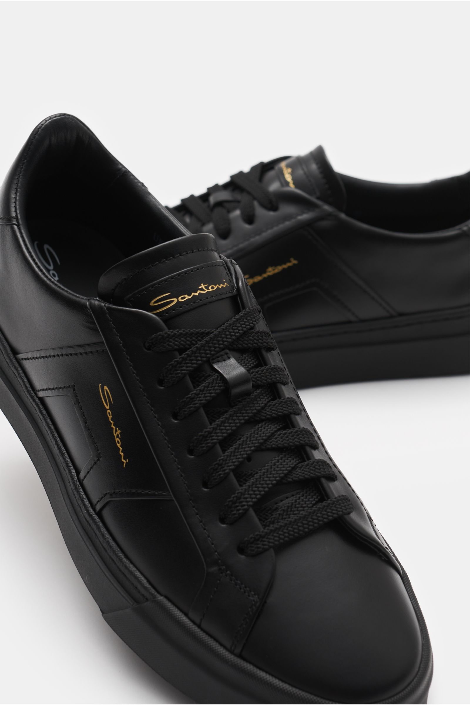 Santoni Sneaker 'Double Buckle' schwarz aus edlem Glattleder mit Sieben-Loch-Schnürung, runder Vorderkappe, tonalen Overlays und Emblem, Lederfutter, gepolstertem Schaftrand, flexibler Kautschuksohle, Schriftzug auf Laufsohle, frontal nah fotografiert.