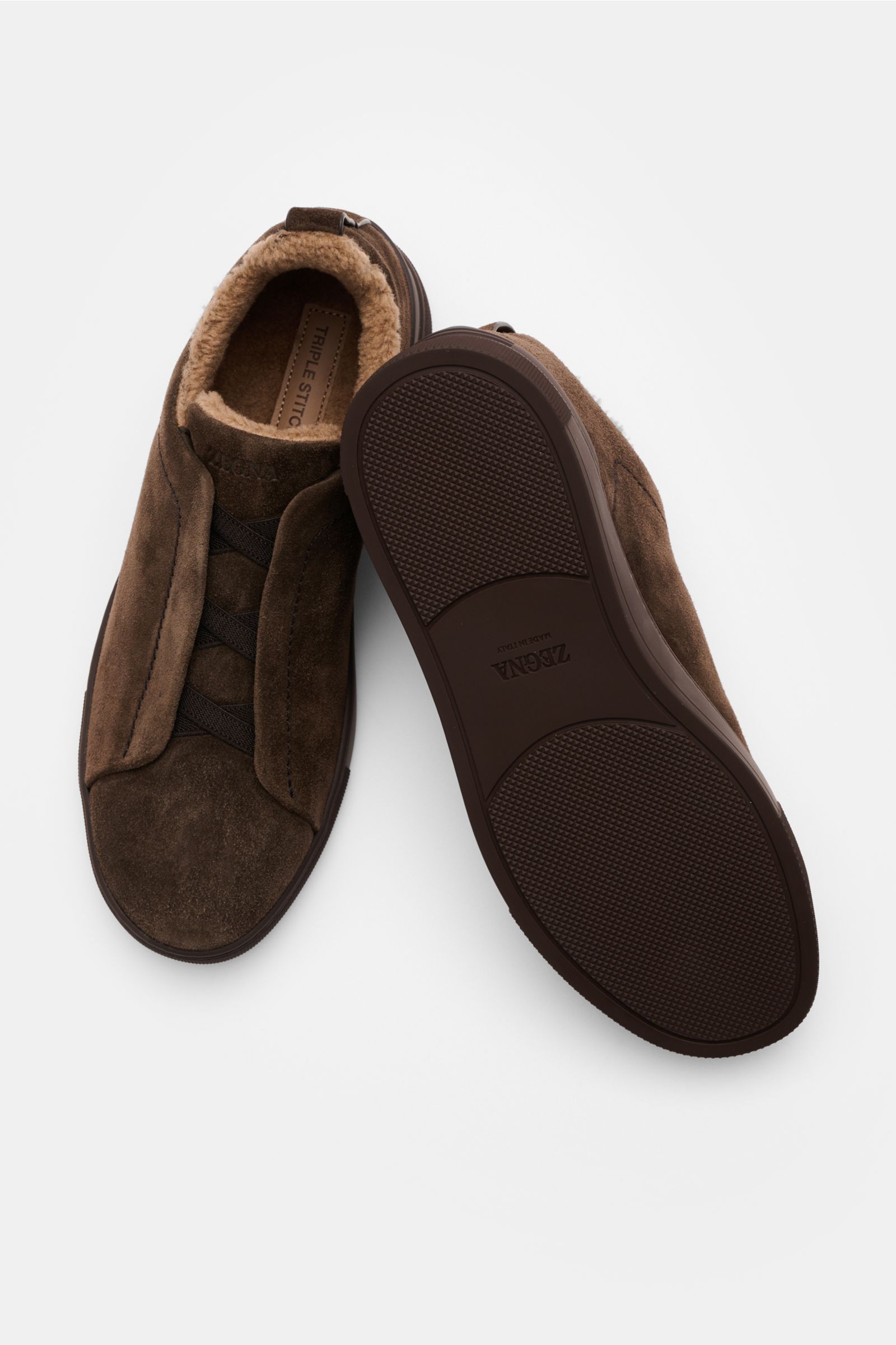 Zegna Slip-on-Sneaker 'Triple Stitch' dunkelbraun, aus edlem Veloursleder, mit elastischen Bändern, Fellimitat-Futter, flexiblem Gummi, Seiten- und Sohlenansicht.
