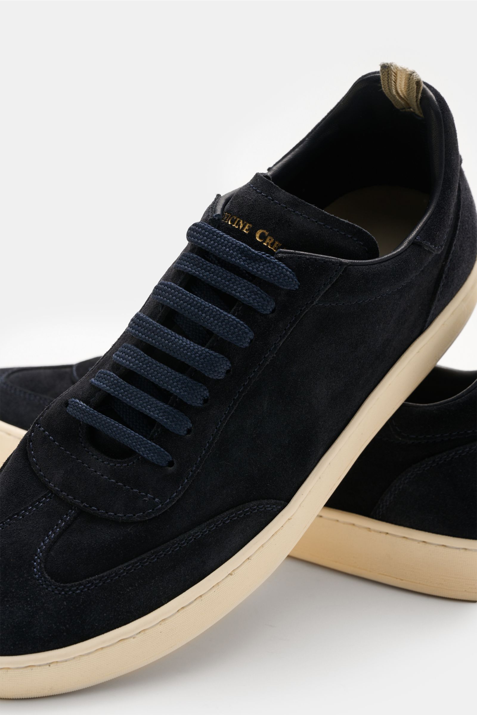Officine Creative Sneakers 'Kafka' navy in premium suede shown from a close-up front-side angle with round toe cap, wing cap, embossed logo on tongue and heel, high padded topline, leather lining, and lightweight cream rubber sole. For anyone who apprecia
