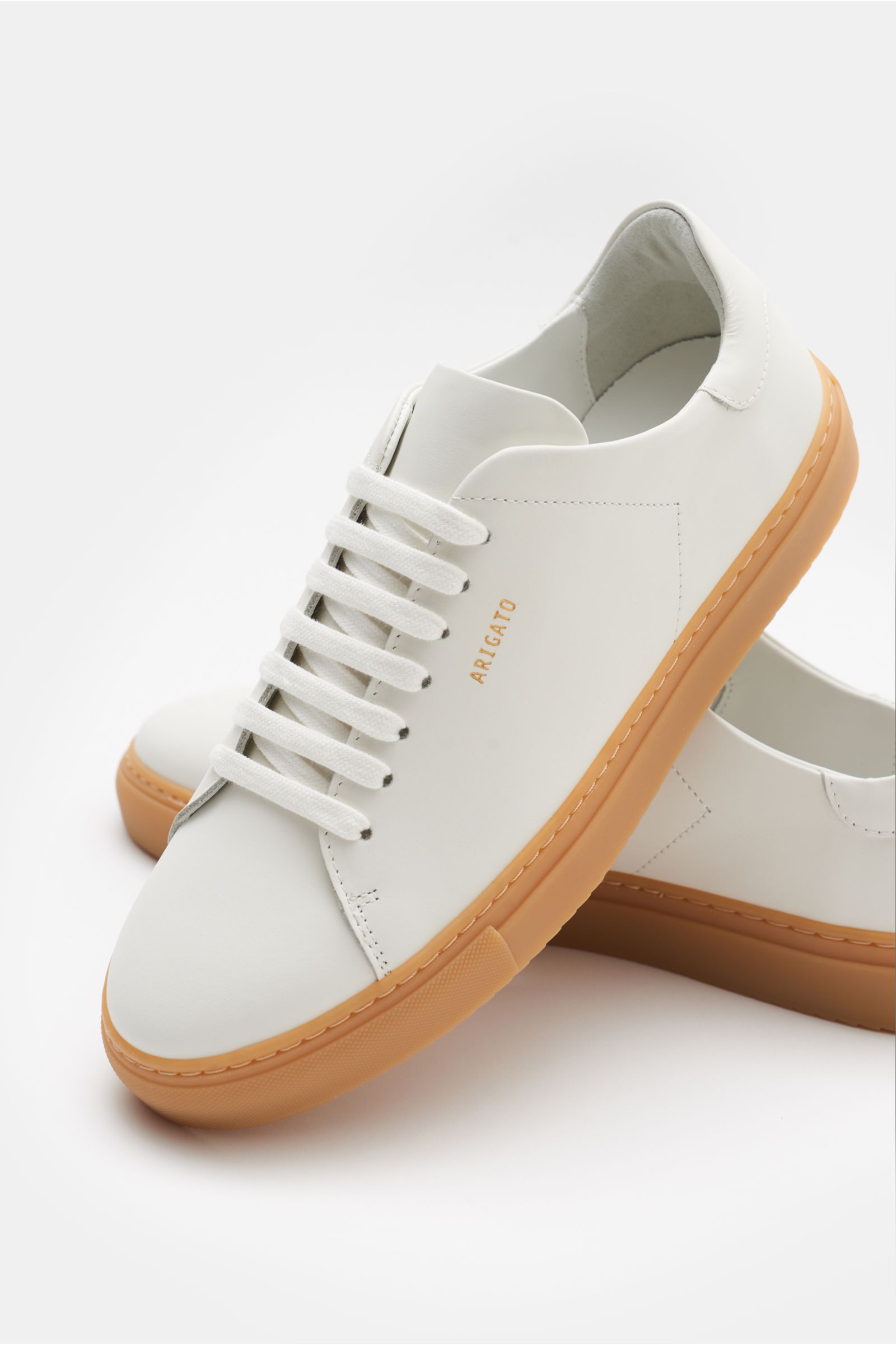 Axel Arigato Sneaker 'Clean 90' offwhite aus edlem Glattleder mit runder Vorderkappe, sieben-Loch-Schnürung, goldfarbener Prägung, gepolstertem Schaftrand, Lederinnenfutter und flexibler Gummisohle, fotografiert aus seitlich-oben.