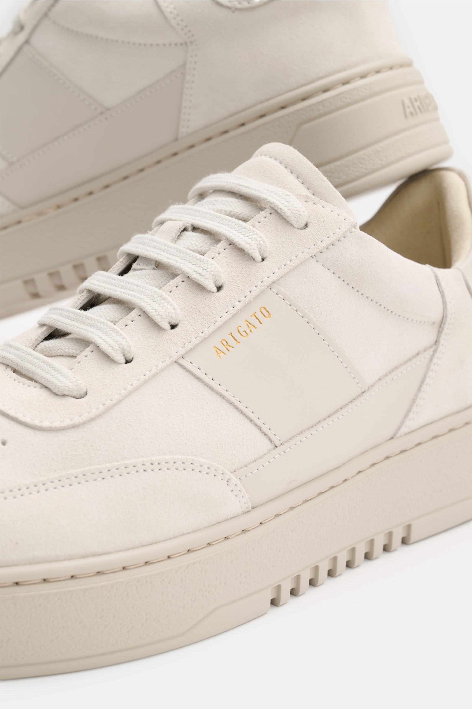 Nahaufnahme von zwei Axel Arigato Sneakern 'Orbit Vintage' beige, aus Veloursleder mit tonalen Overlays, goldfarbener Label-Prägung und flexibler Gummisohle, seitlich und schräg von vorne fotografiert.