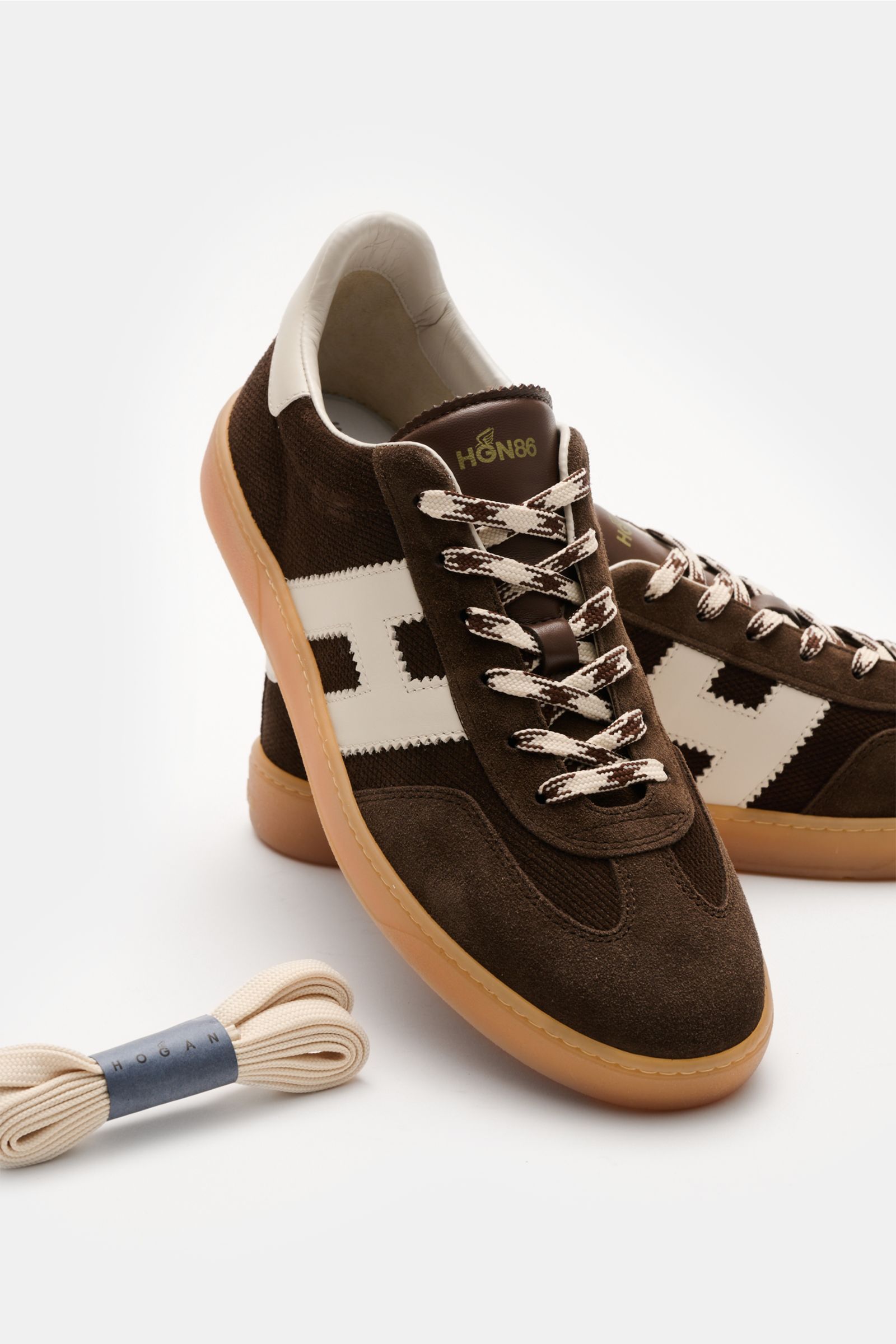 Front angled view of the Hogan Sneaker 'Allacciato' dunkelbraun/weiß showing dark brown embossed suede, six-hole lacing, logo-printed tongue, padded collar, H-shaped brand initial, leather and textile lining, memory foam insole, and flexible gum sole, wit