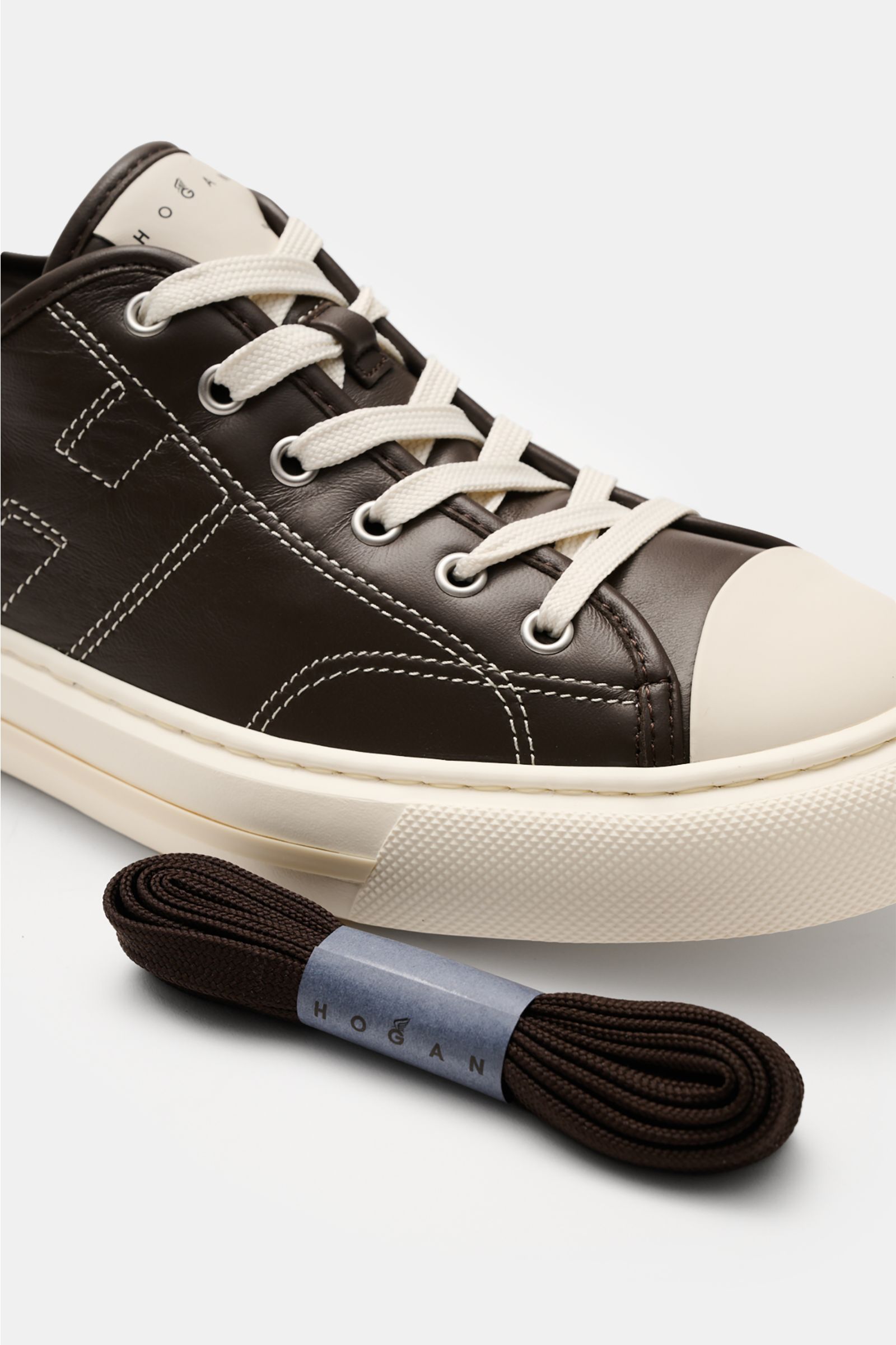 Close-up side view of Hogan Sneaker 'Allacciato Cuciture' dunkelbraun/offwhite with smooth leather, seven-eyelet lacing, logo tongue, H-shaped brand initial, leather/textile lining, memory foam footbed, flexible rubber sole, and extra dark brown laces.