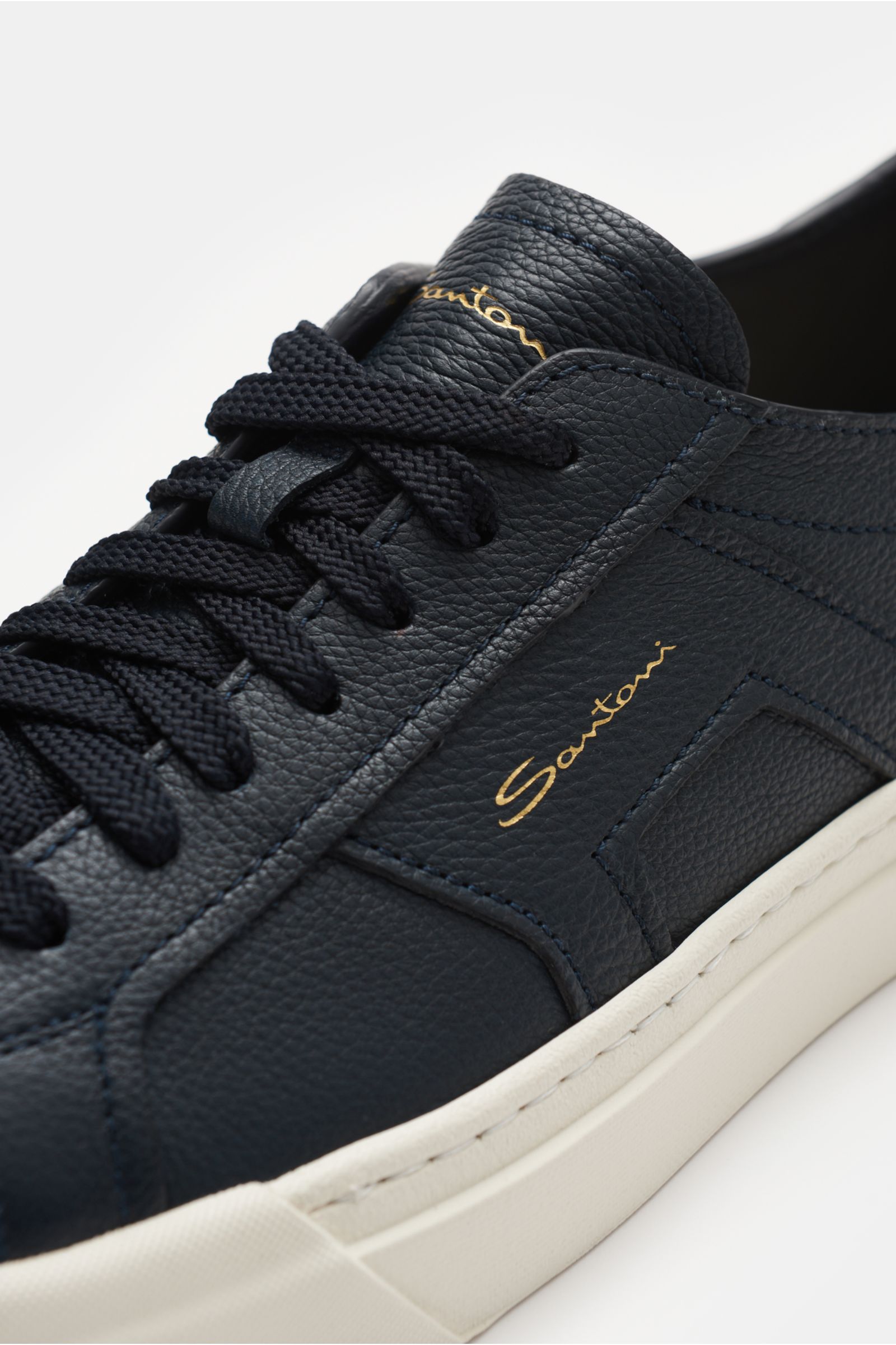 Nahaufnahme des Santoni Sneaker 'Double Buckle' dark navy von schräg oben rechts, fein genarbtes Leder, seitliche Overlays, Sieben-Loch-Schnürung, Emblem auf der Lasche.