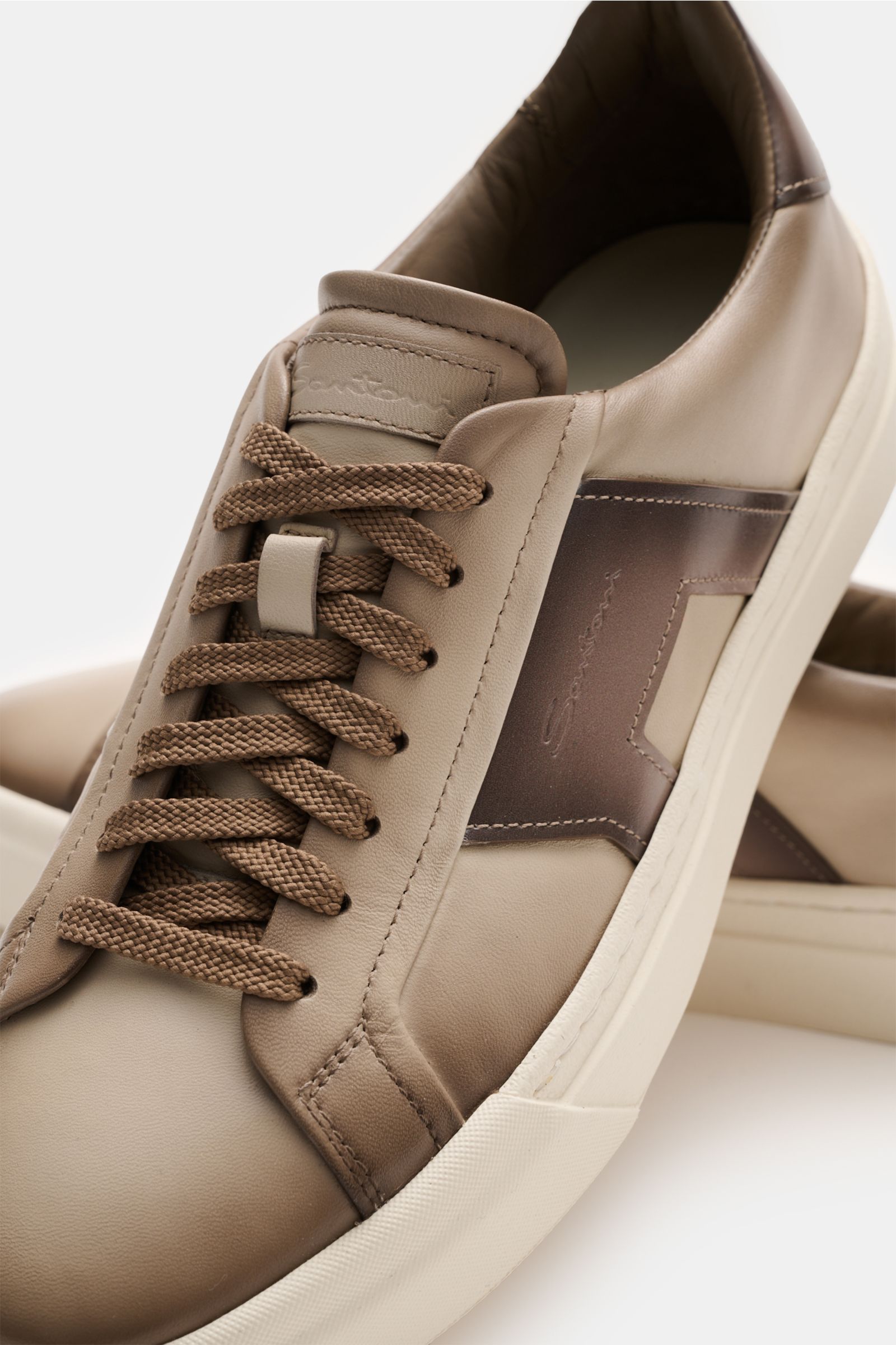 Close-up front-side view of the Santoni Sneaker 'Double Buckle' taupe made of fine smooth leather with seven-hole lacing, padded collar, leather lining, and flexible rubber sole, featuring characteristic double buckle overlays inspired by classic monkstra