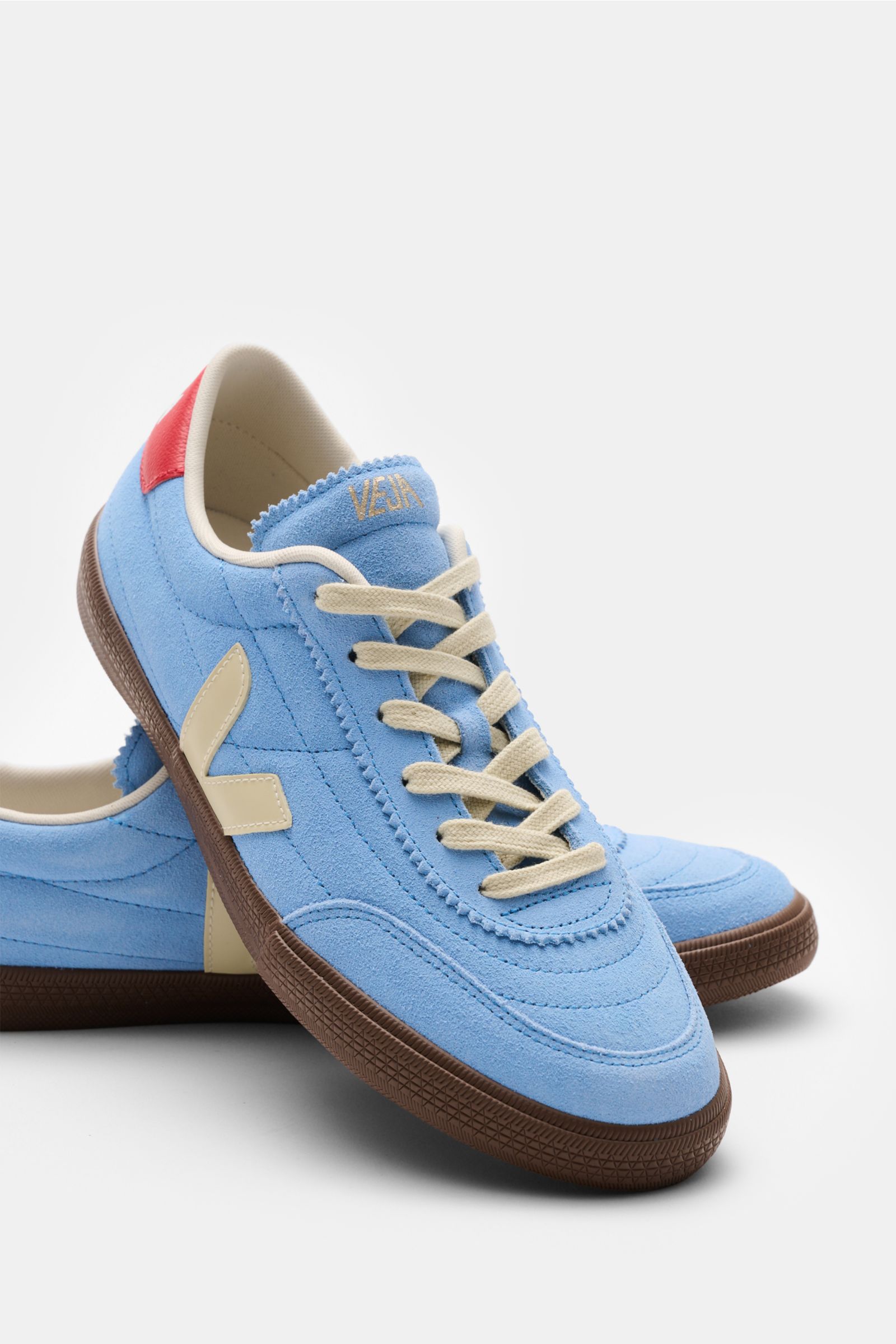 Veja Sneakers 'Panenka' blue/red/cream shown from a front-side angle, made of smooth blue suede with cream leather overlays, six-eyelet lacing, padded topline with logo, textile lining, and flexible brown rubber sole, featuring a red heel tab and tongue w