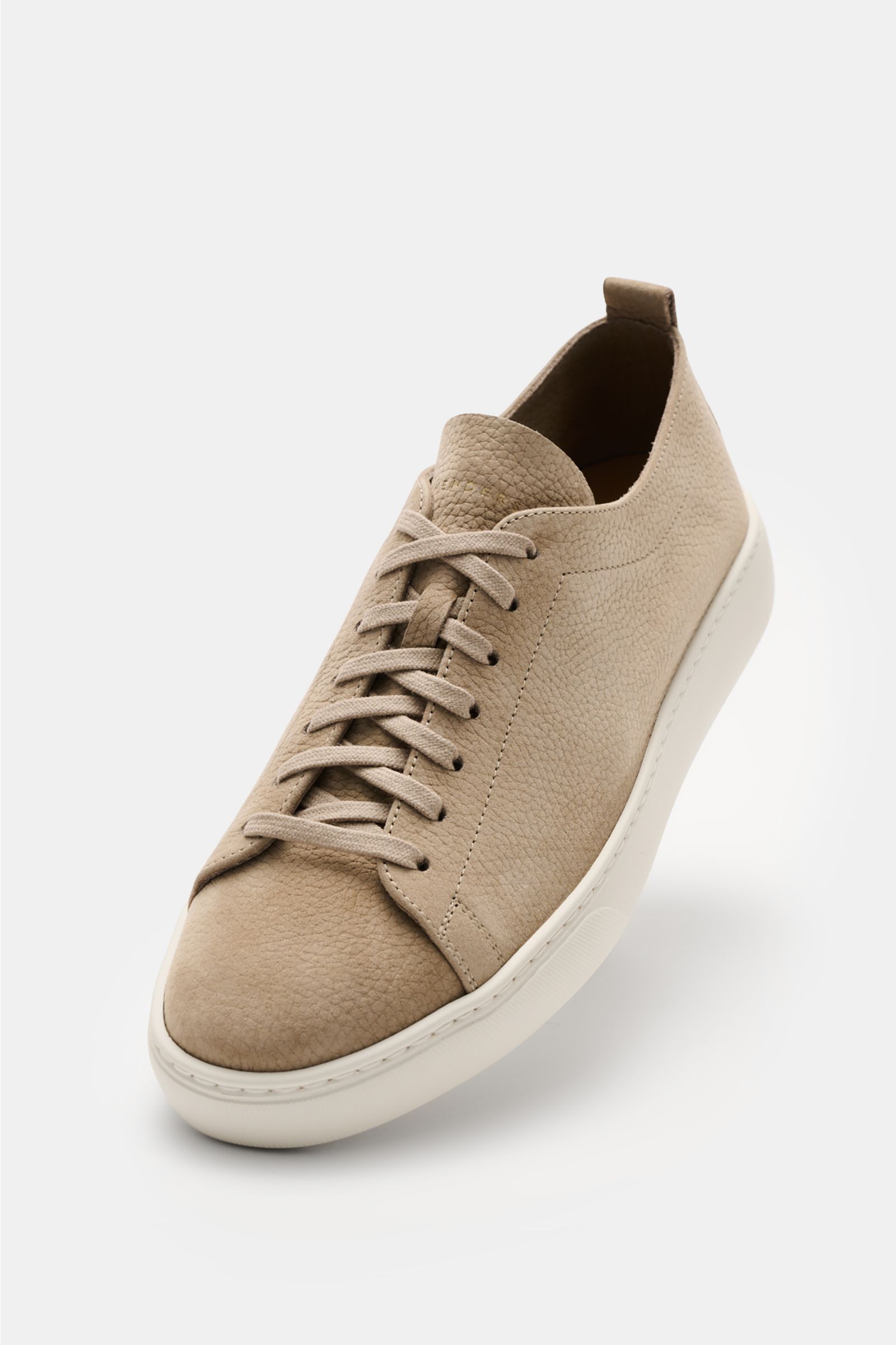 Henderson Sneaker 'Thomas' taupe shown from a front diagonal view, made of soft brushed leather with round toe, seven-eyelet lacing, logo emboss on tongue, leather lining, pull tab, and lightweight white rubber sole. Ultra leichte handwerkliche Perfektion