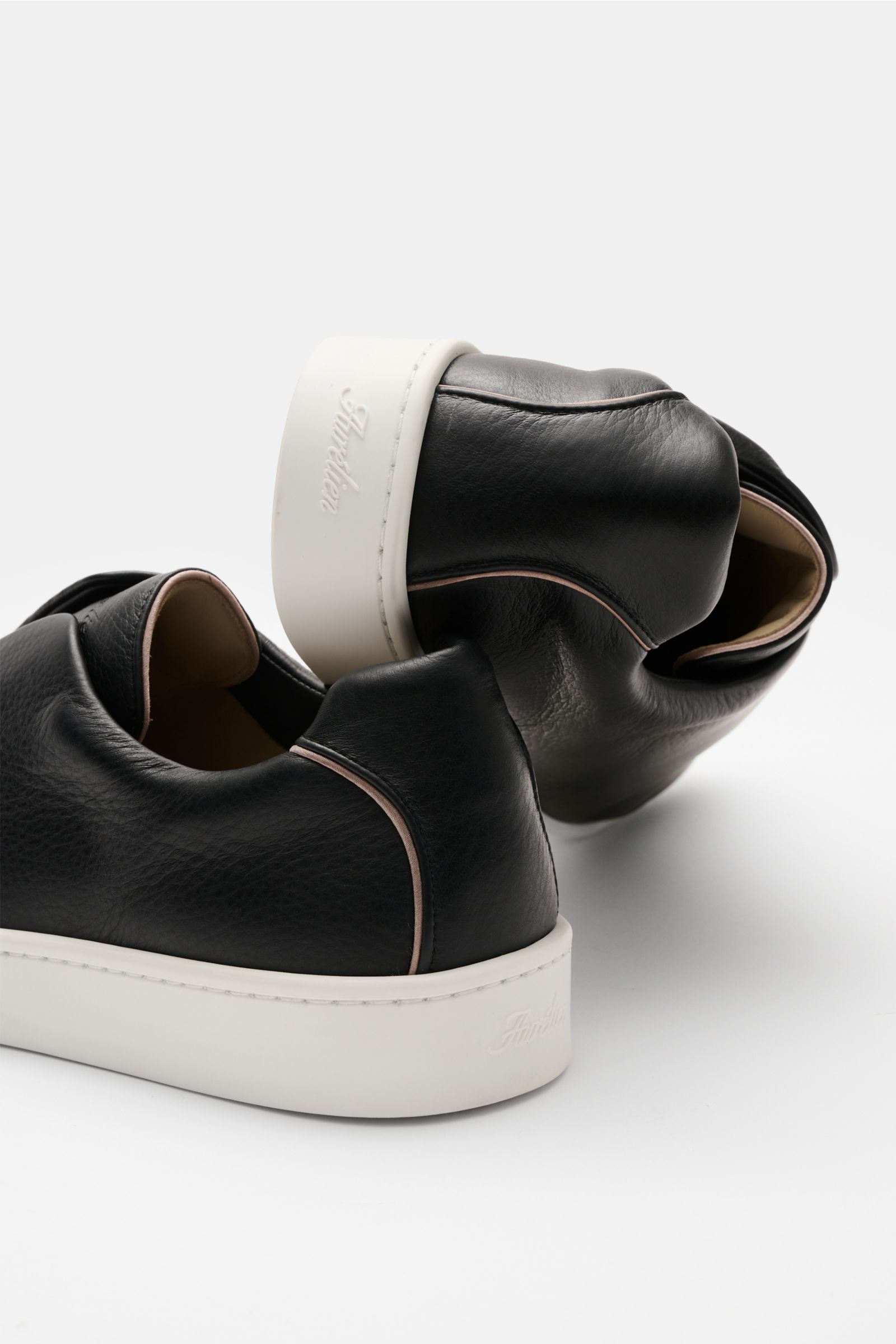 Aurélien Slip-on-Sneaker schwarz, seitlich und von hinten fotografiert, fein genarbtes Leder, elastische Bänder, gepolsterter Schaftrand, flexible weiße Gummisohle.