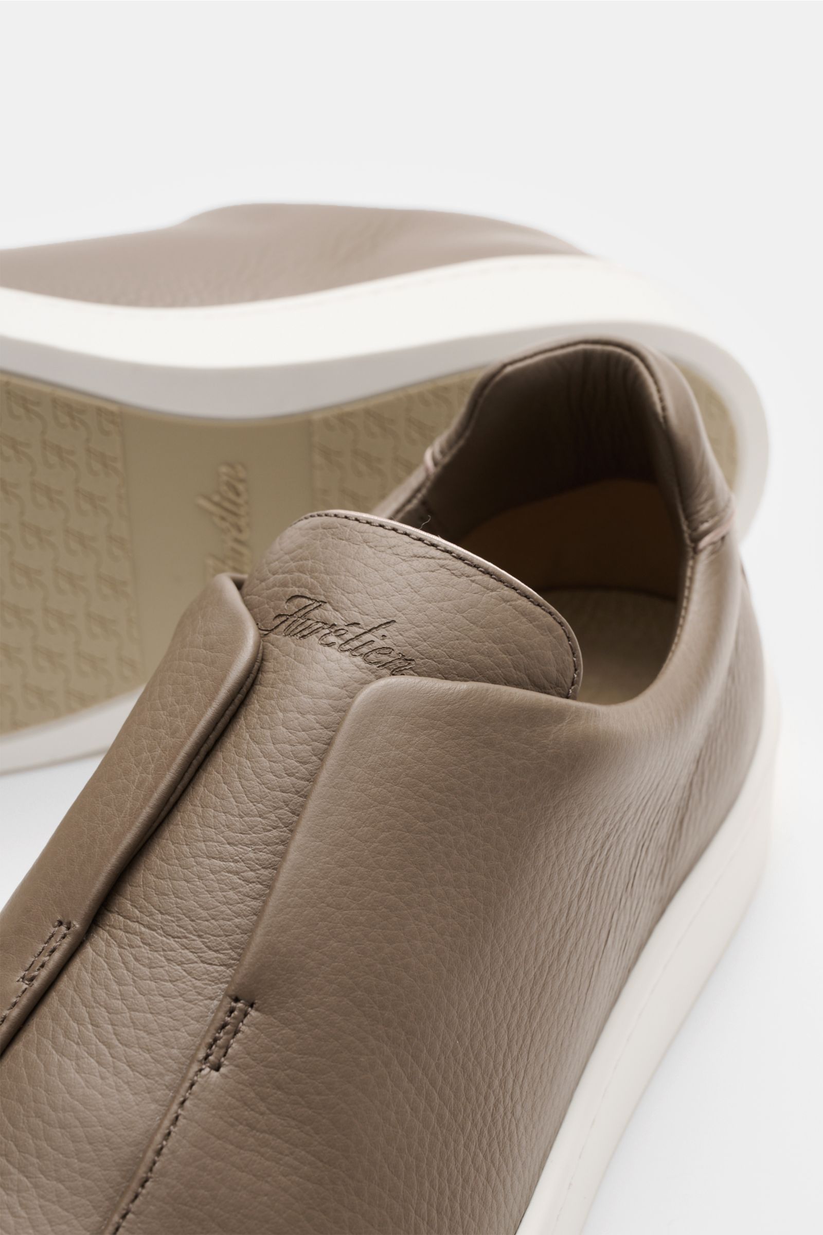 Aurélien Slip-on-Sneaker taupe, nah von oben fotografiert, fein genarbtes Leder, runde Vorderkappe, elastische Bänder, gepolsterter Schaftrand, dezente Logo-Prägung, Innenfutter Leder, flexible weiße Gummisohle.