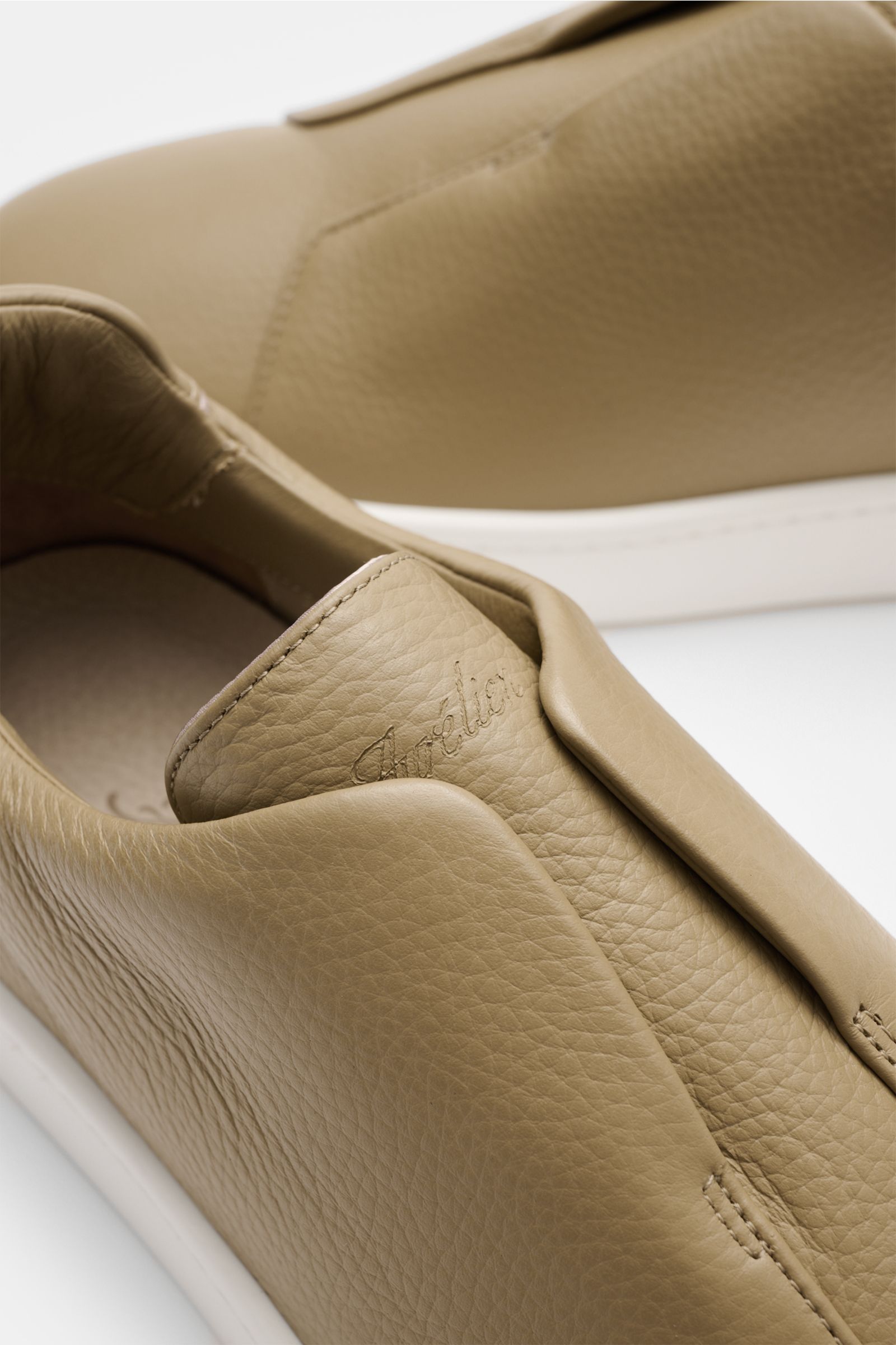 Aurélien Slip-on-Sneaker hellbraun in Nahaufnahme von oben, fein genarbtes Leder, runde Vorderkappe, elastische Bänder, gepolsterter Schaftrand, dezente Logo-Prägung, flexible weiße Gummisohle.