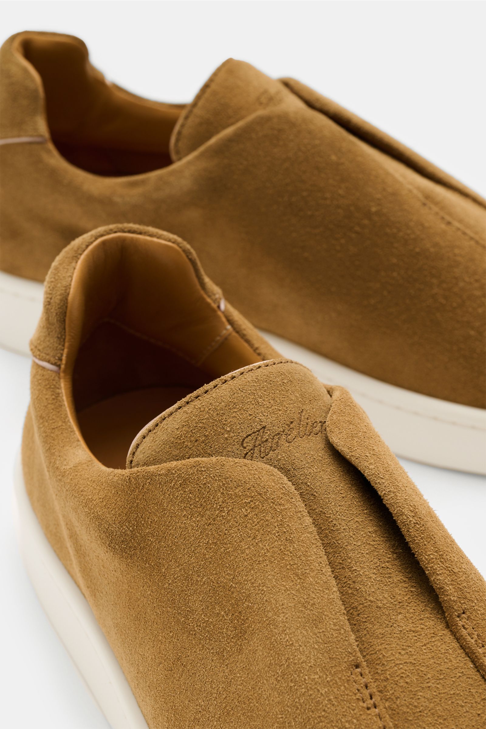 Nahaufnahme aus schräger Perspektive des Aurélien Slip-on-Sneaker camel aus softem Veloursleder mit runder Vorderkappe, elastischen Bändern, hohem Schaftrand, dezenter Logo-Prägung, Leder-Innenfutter und flexibler Gummisohle.