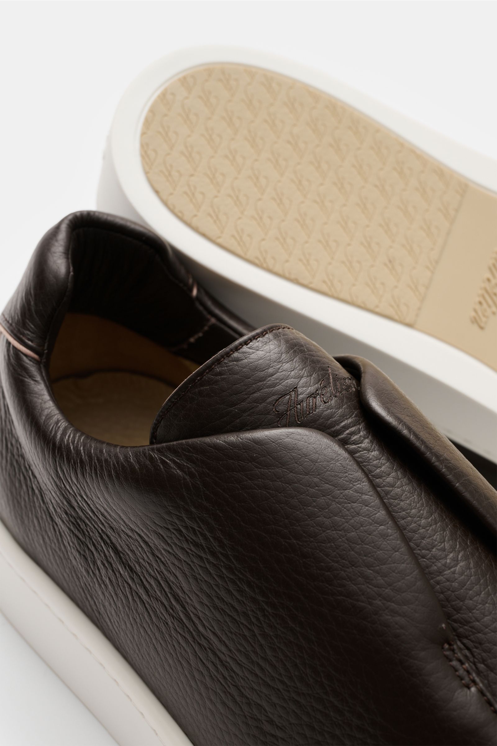 Aurélien Slip-on-Sneaker dunkelbraun shown from a close-up side and bottom perspective, featuring finely grained leather, round toe cap, hidden elastic bands, high padded collar, subtle logo embossing, leather lining, and flexible rubber sole. Minimalist 