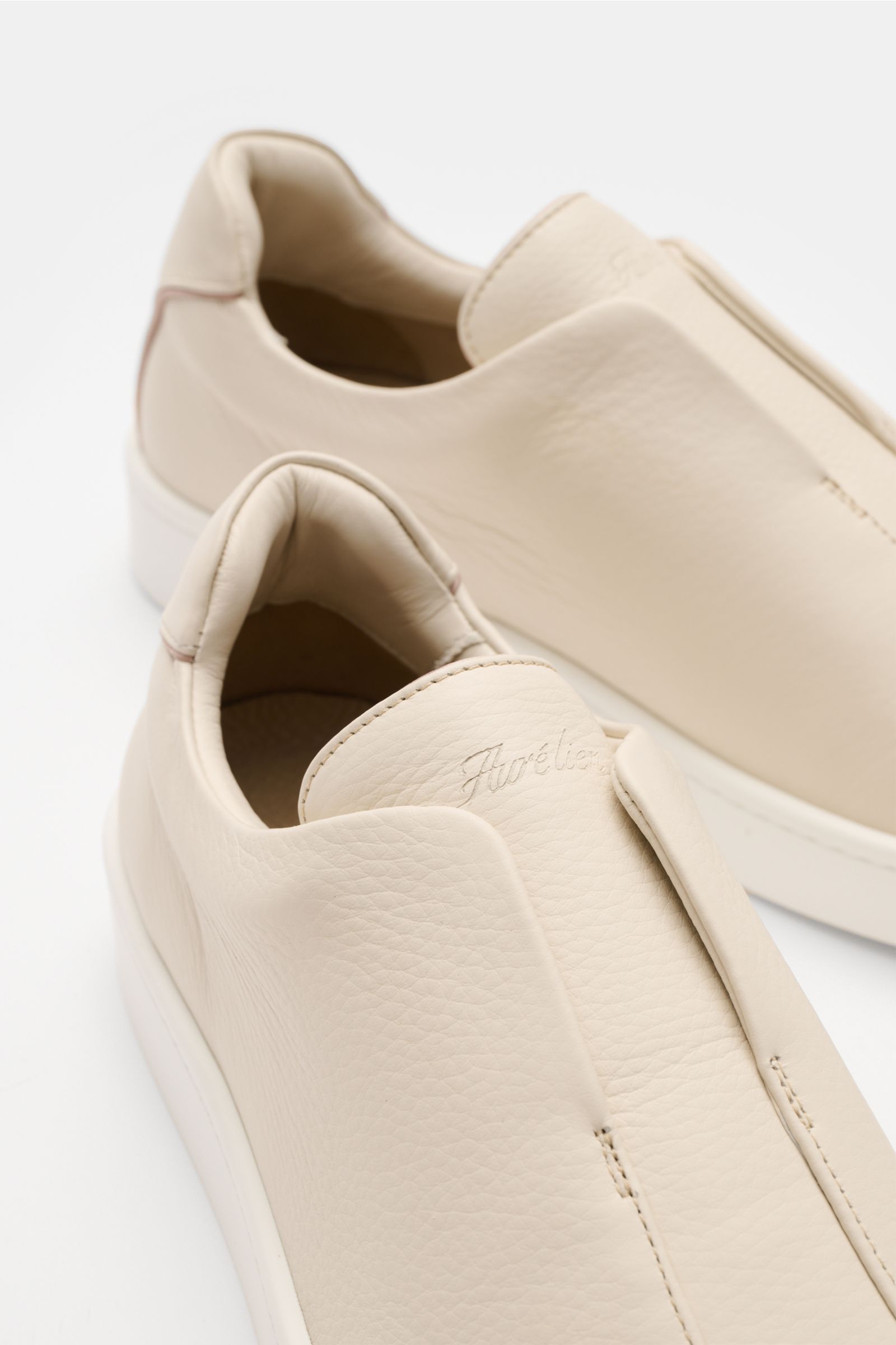 Close-up front-side view of Aurélien Slip-on-Sneaker creme in finely grained leather with rounded toe, elastic bands, padded collar, subtle logo embossing, leather lining, and flexible rubber sole. Minimalist design paired with exceptional craftsmanship: 