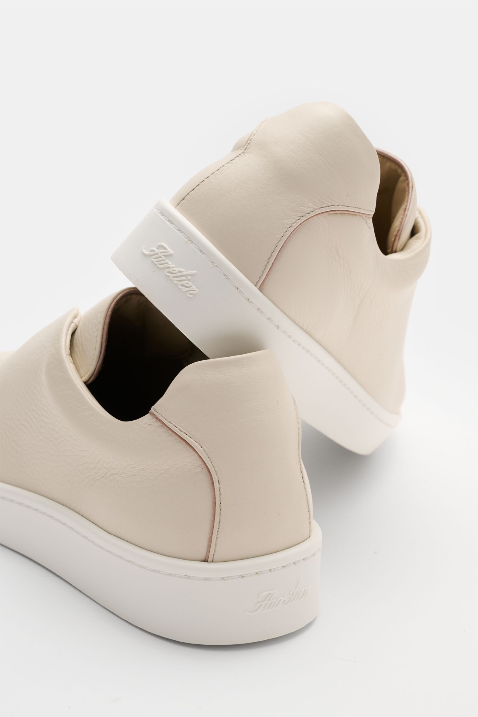 Rear and side view of Aurélien Slip-on-Sneaker creme, featuring minimalist design, finely grained leather, round toe, elastic bands, padded collar, subtle logo embossing, leather lining, and flexible rubber sole. Minimalistisches Design gepaart mit außerg