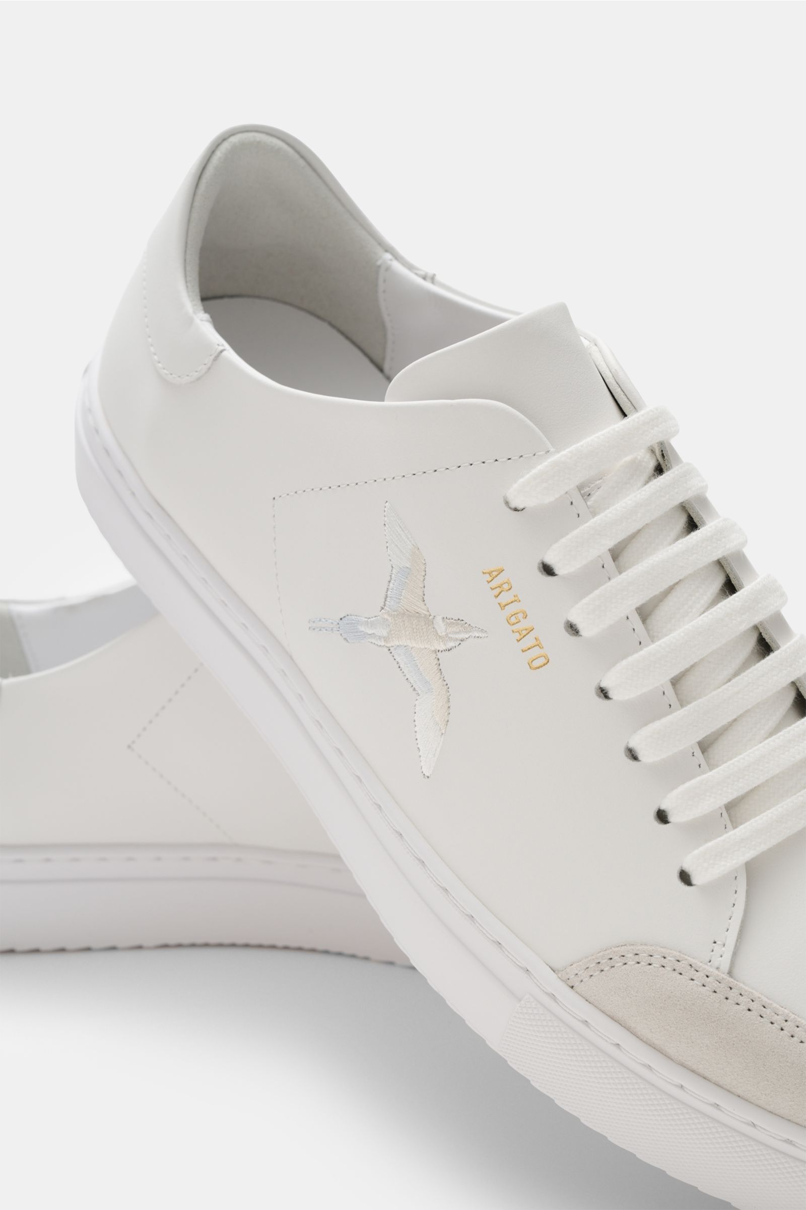 Weiße Nahaufnahme des Axel Arigato Sneaker 'Clean 90' mit Glattleder, Kolibri-Stickerei, Velours-Overlay und flexibler Sohle, seitlich fotografiert.