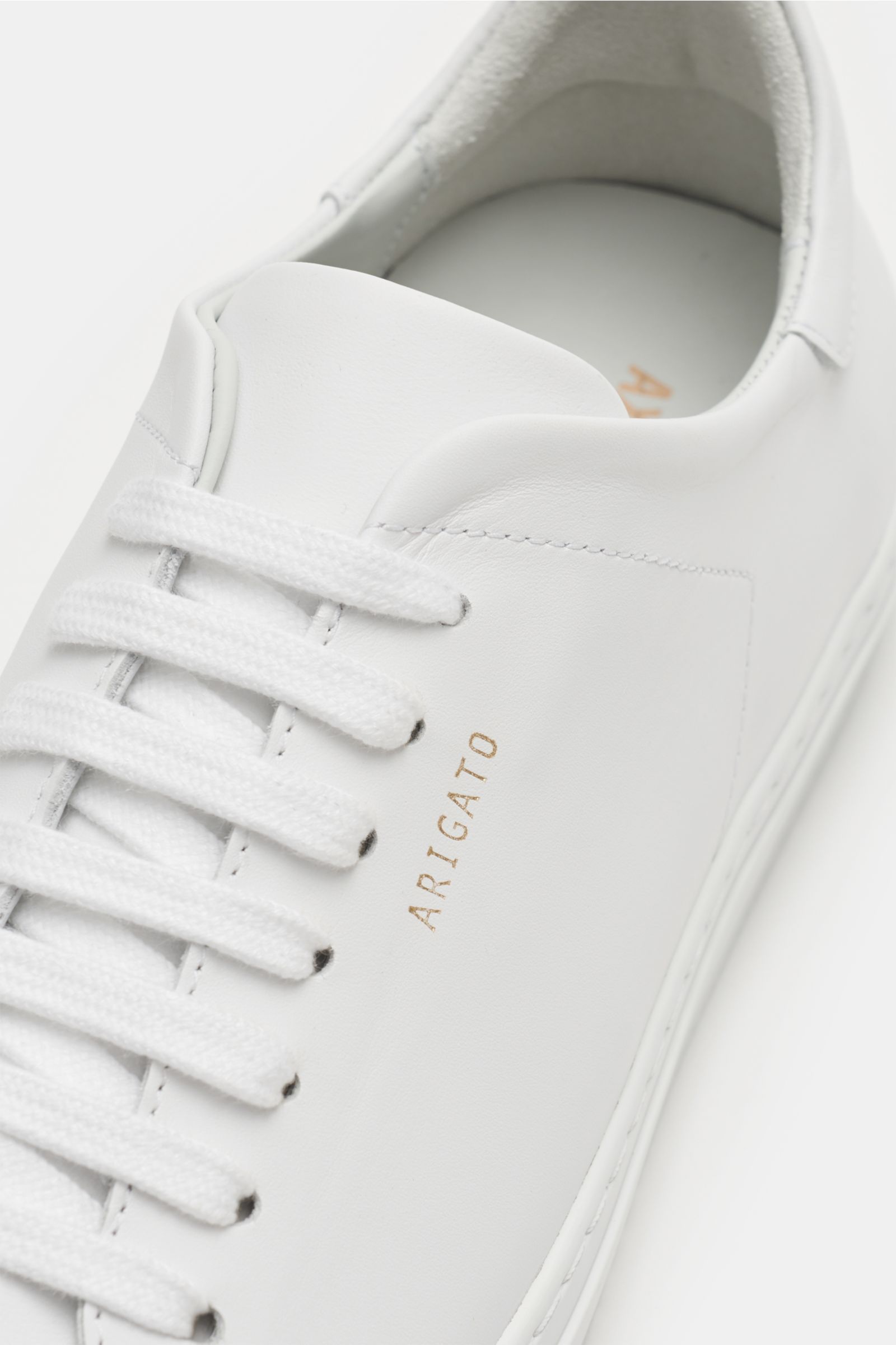 Nahaufnahme des Axel Arigato Sneaker 'Clean 90' weiß von schräg oben, zeigt Glattleder, sieben-Loch-Schnürung und goldfarbene Prägung.