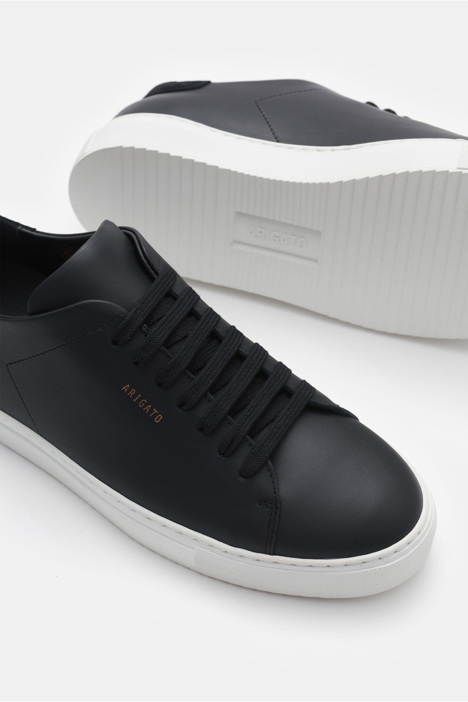 Axel Arigato Sneaker 'Clean 90' schwarz aus edlem Glattleder mit Veloursleder-Detail, runder Kappe, Sieben-Loch-Schnürung, goldfarbener Prägung, gepolstertem Schaftrand, Lederfutter und flexibler Gummisohle, seitlich und von unten fotografiert.