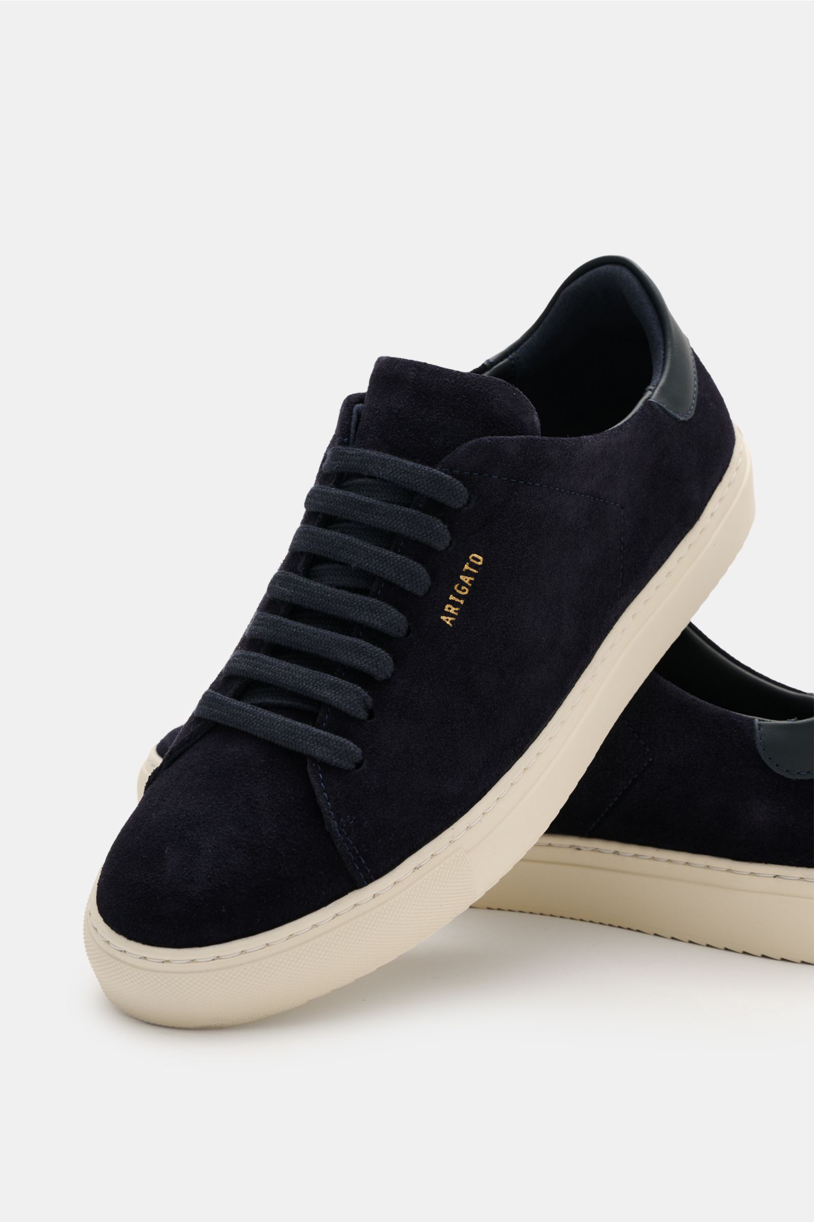 Axel Arigato Sneaker 'Clean 90 Suede' navy aus softem Veloursleder, runde Vorderkappe, Sieben-Loch-Schnürung, seitlich goldfarbene Prägung, gepolsterter Schaftrand, Leder-Innenfutter, flexible Gummisohle, frontal schräg fotografiert.