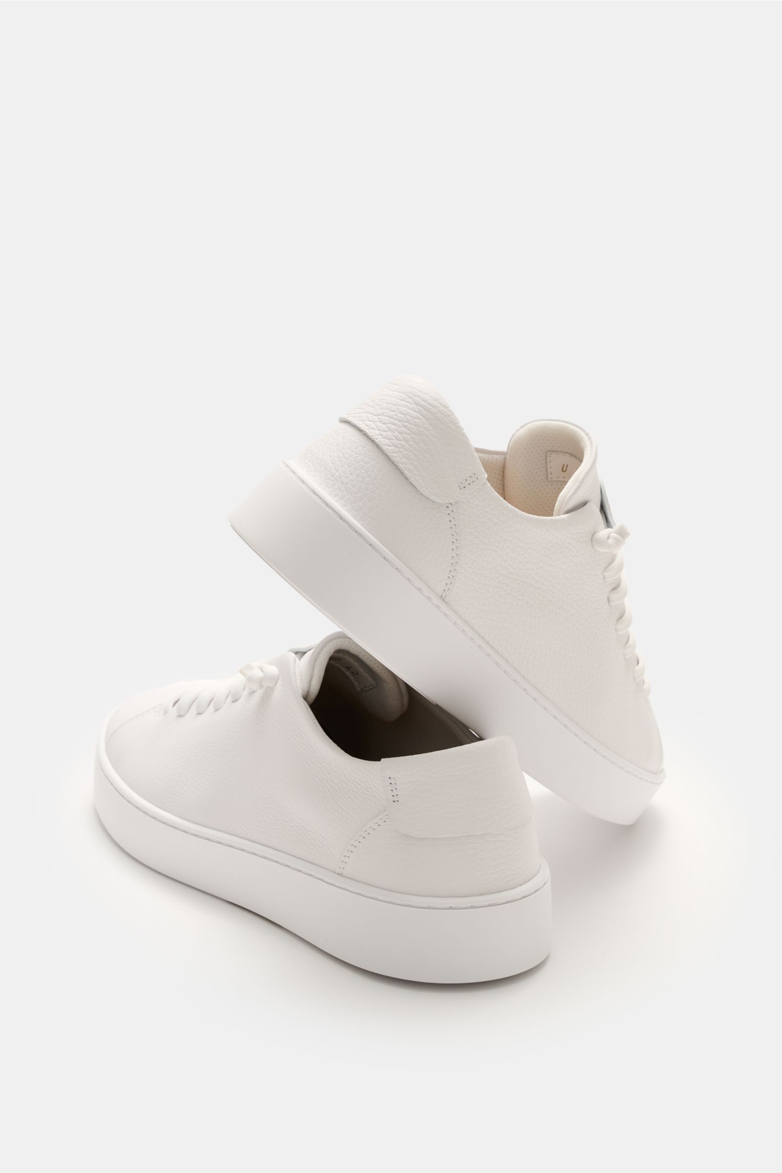 Two Fabiano Ricci Sneaker weiß photographed from a rear side angle showing soft, grained white leather, round toe, elastic seven-eyelet lacing, logo-embossed tongue, mesh lining, removable padded insole, and flexible white rubber sole.