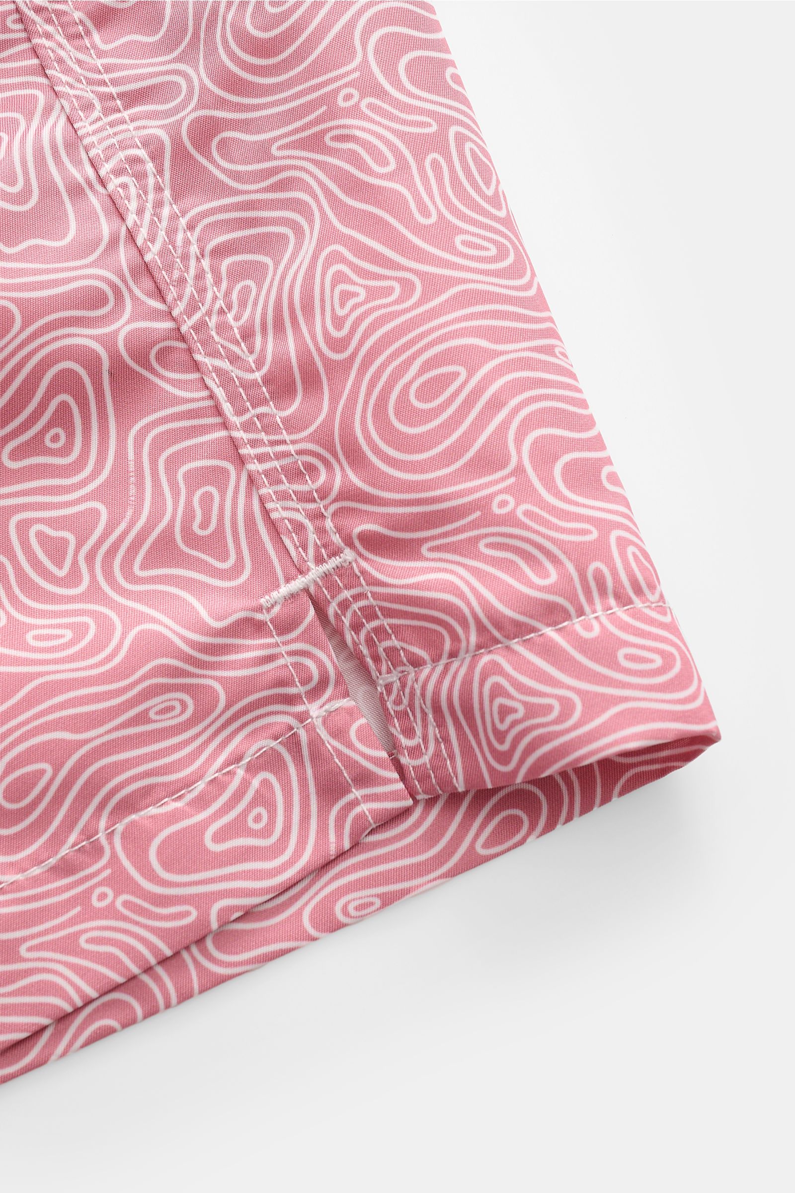 Close-up of the hem and side seam from a top-down perspective, showing the white contour map pattern on hellrot fabric of the 04651/ A trip in a bag Badeshorts 'Seamap' hellrot/weiß gemustert made of quick-drying microfiber with short side slits.