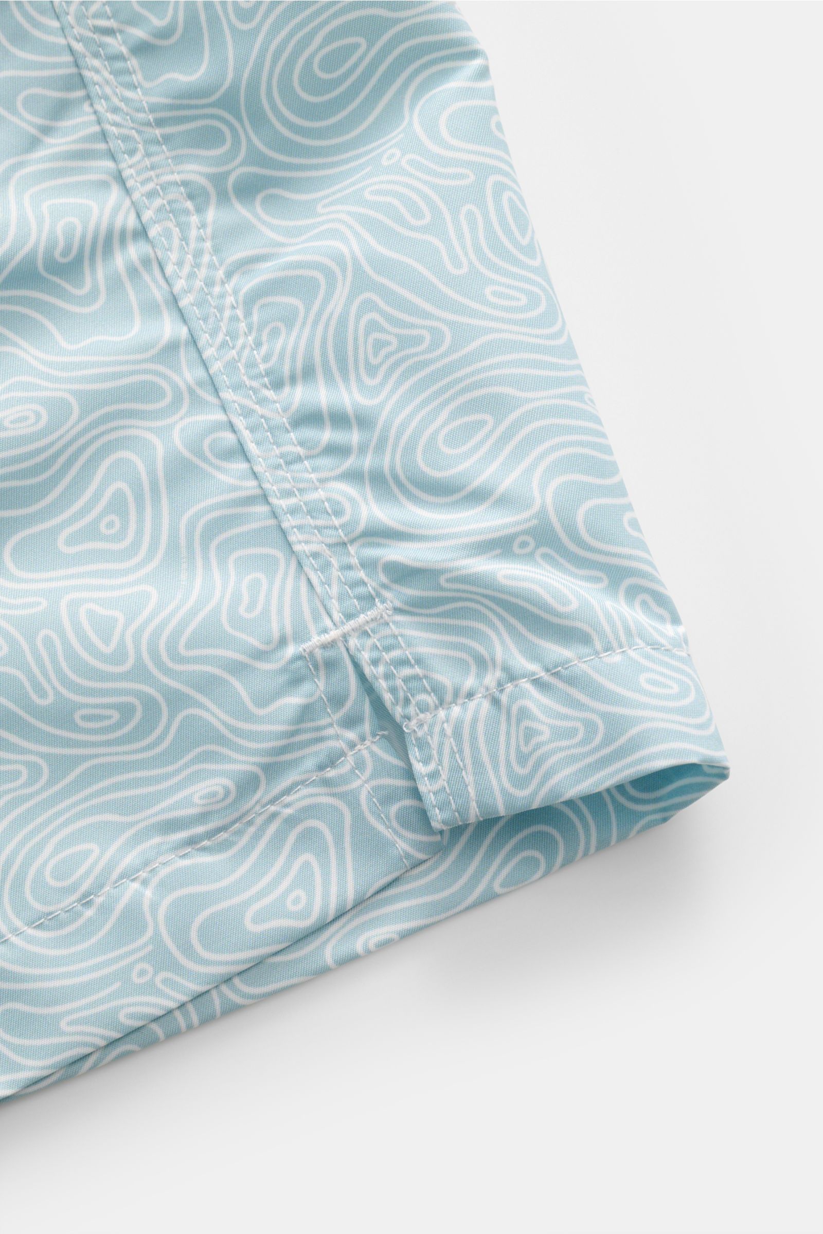 Close-up of the lower hem and side seam of the 04651/ A trip in a bag Badeshorts 'Seamap' mint/weiß gemustert, showing the quick-drying microfiber fabric with a white contour map pattern, regular fit with short side slits, photographed from an angled top-