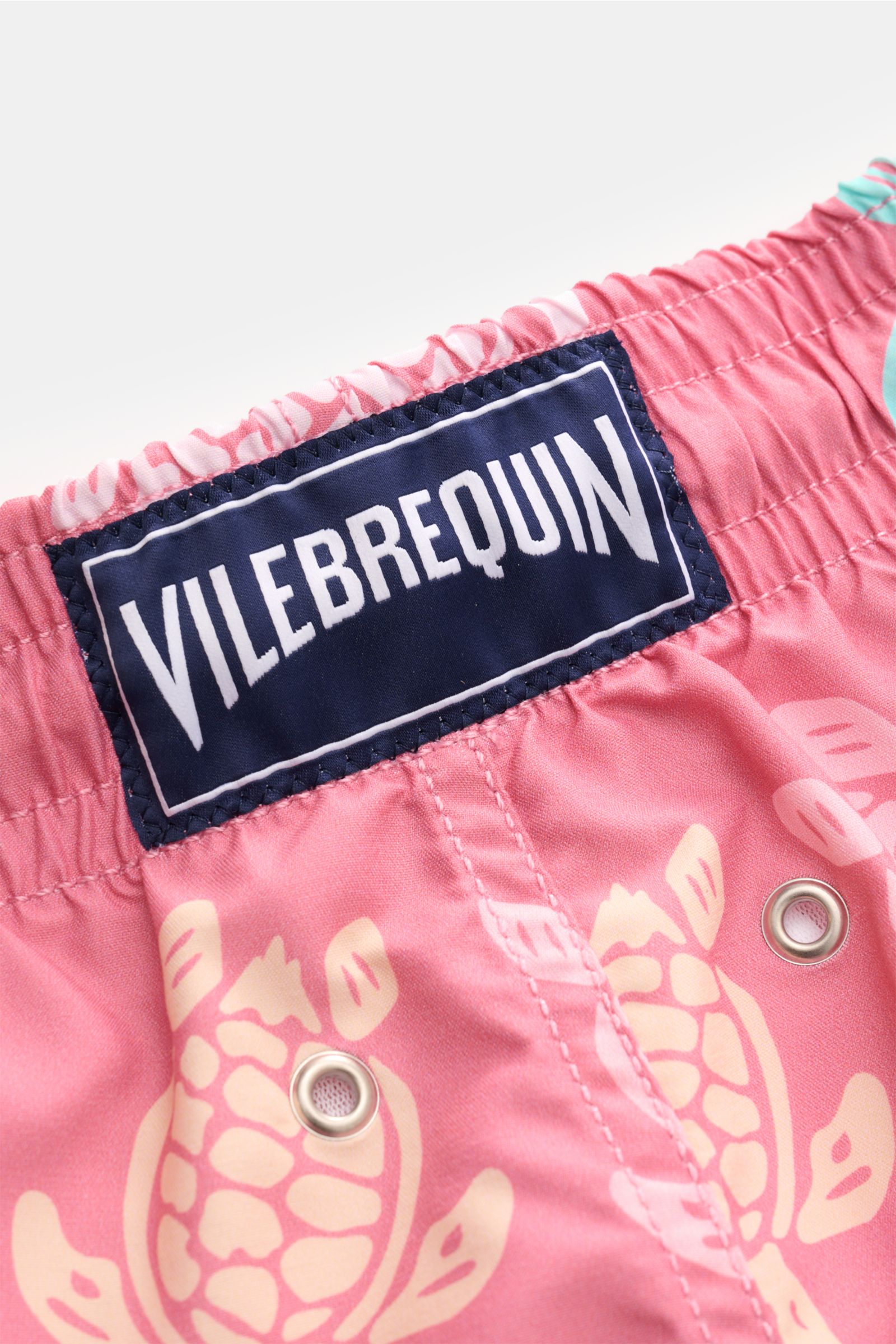 Close-up view of the back waistband of Vilebrequin Swim shorts 'Moorea' rose/mint/yellow patterned, showing elastic waistband, VILEBREQUIN label, drainage eyelets, and turtle print on high-quality microfibre fabric.