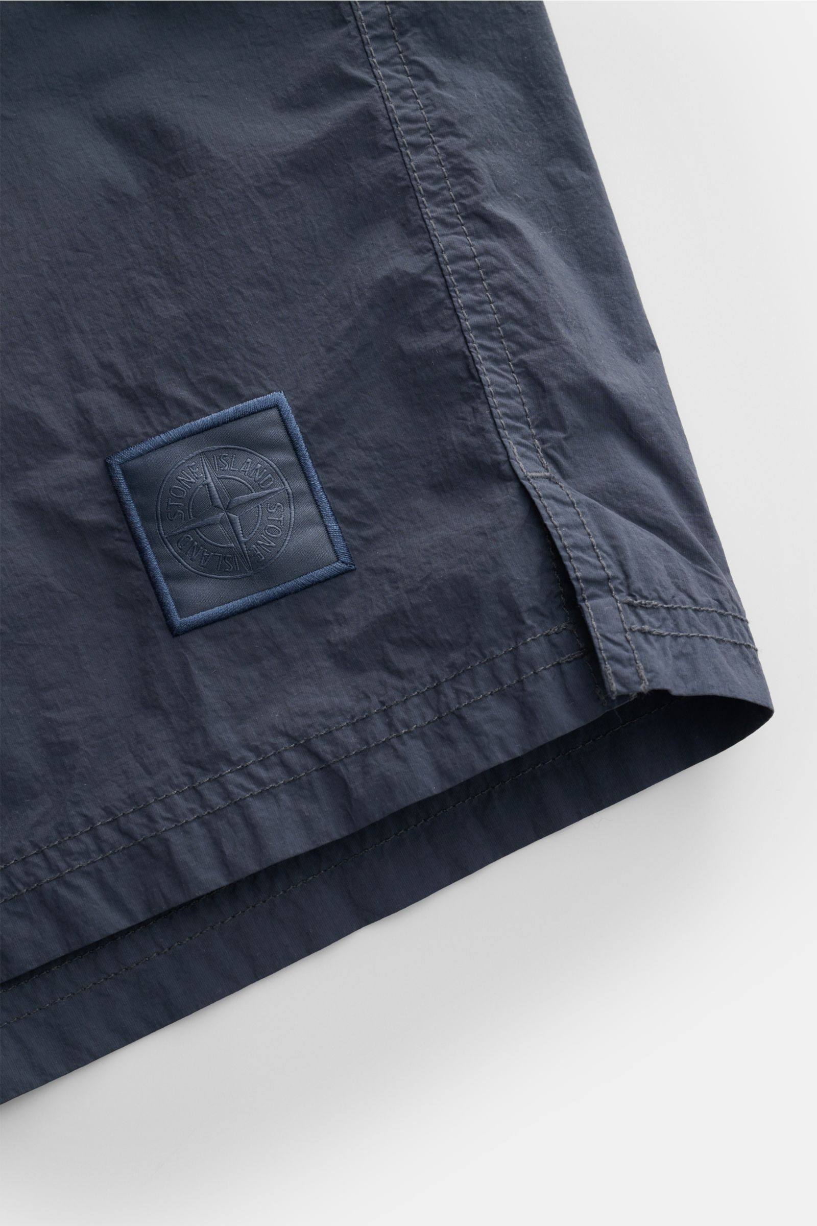 Stone Island Badeshorts 'Ghost Piece' graublau, Detailaufnahme Saum und Logo, hochwertige Microfaser, Regular Fit, elastischer Bund, Mesh-Innenfutter.