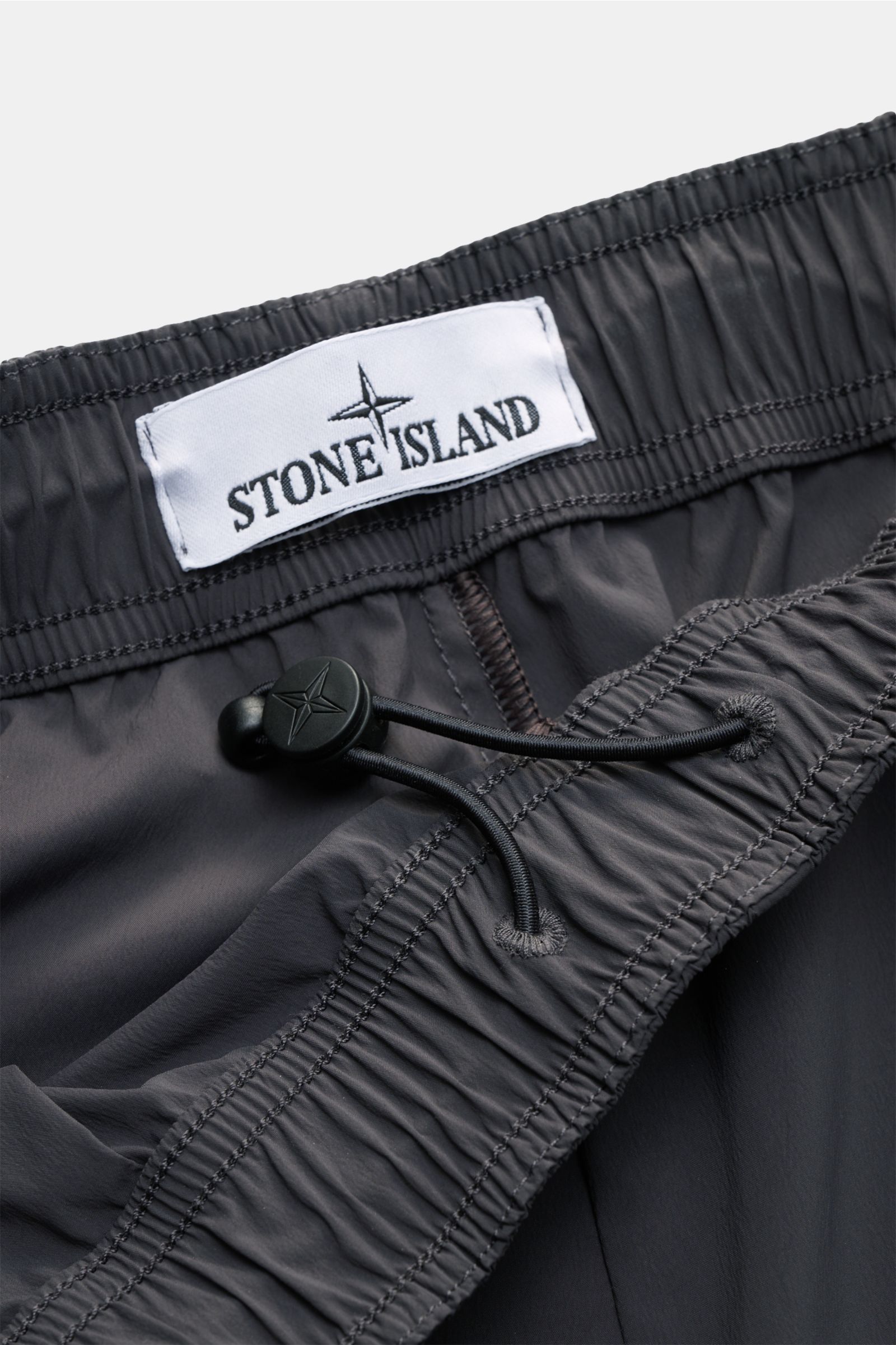 Stone Island Shorts 'Stellina' dunkelgrau, Detailaufnahme des elastischen Bundes mit innenliegendem Tunnelzug und weißem Stone Island Label, Microfaser, Loose Fit, Stern-Stitching.