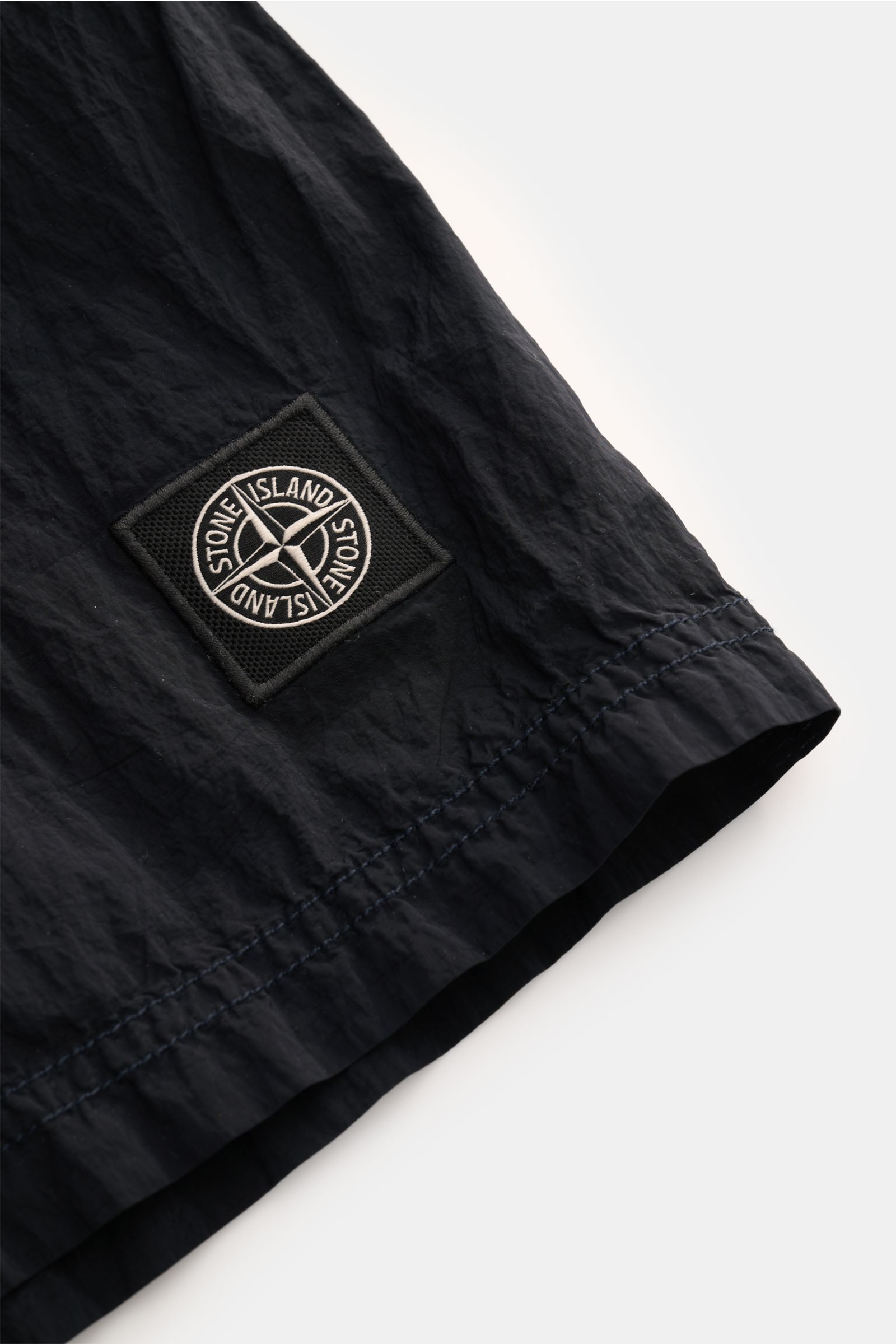 Stone Island Badeshorts dark navy aus recycelter Microfaser, Detailaufnahme am Saum mit Weblabel aus schräger Perspektive.