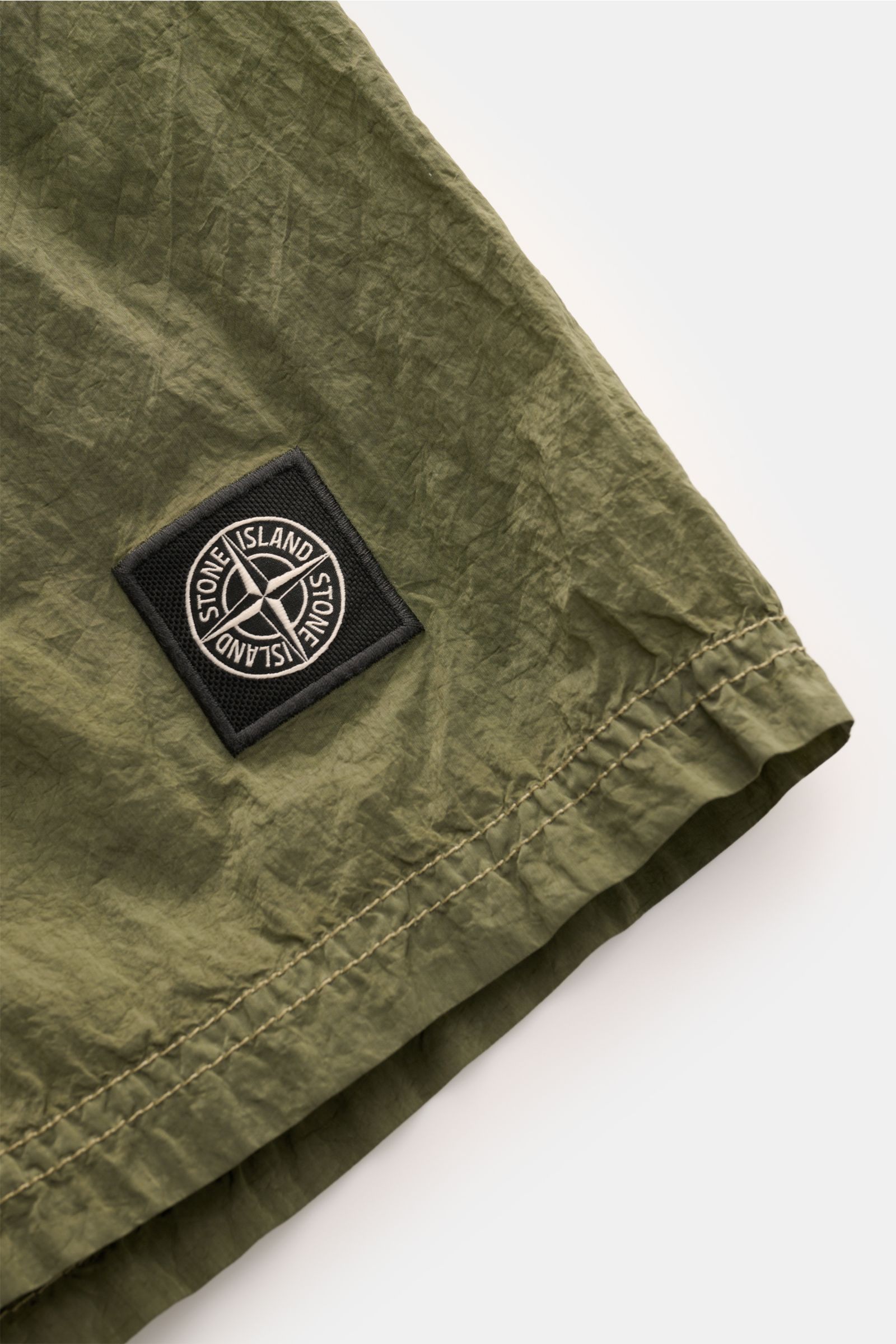 Stone Island Badeshorts oliv, Nahaufnahme vom unteren Bein mit gestepptem Saum und schwarzem Marken-Logo, recycelte Microfaser.