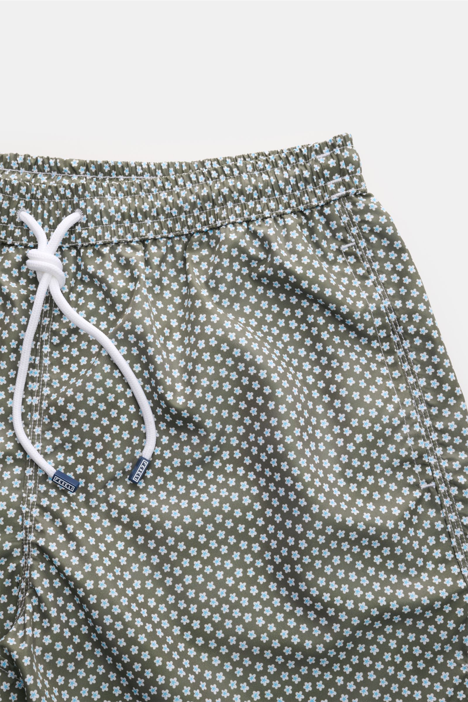 Close-up front view of Fedeli Swim shorts 'Madeira Airstop' green/white/light blue patterned with elasticated waistband, white drawstring, and floral print.

Description:  
An essential for your summer vacation: These FEDELI swim shorts have an express