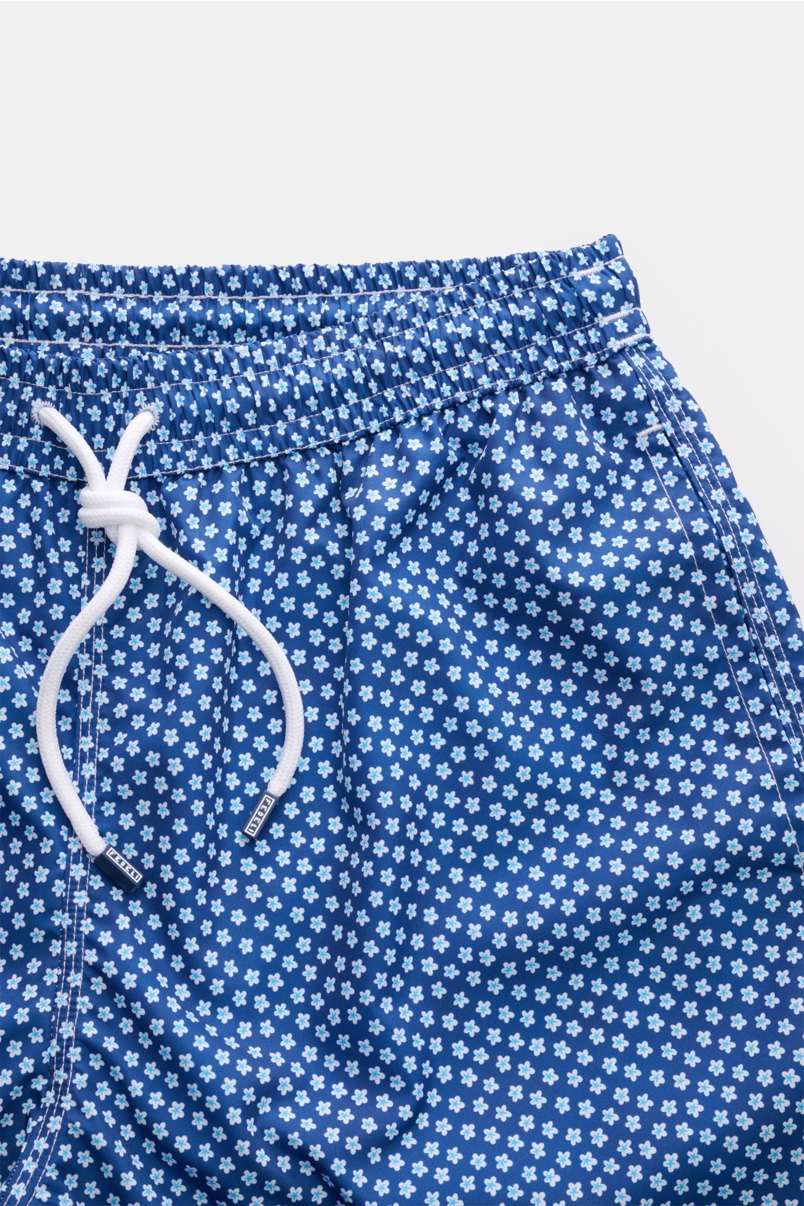 Close-up front view of Fedeli Swim shorts 'Madeira Airstop' blue/white/light blue patterned with elastic waistband and white drawstring, featuring small floral design.

Description: An essential for your summer vacation: These FEDELI swim shorts have an e