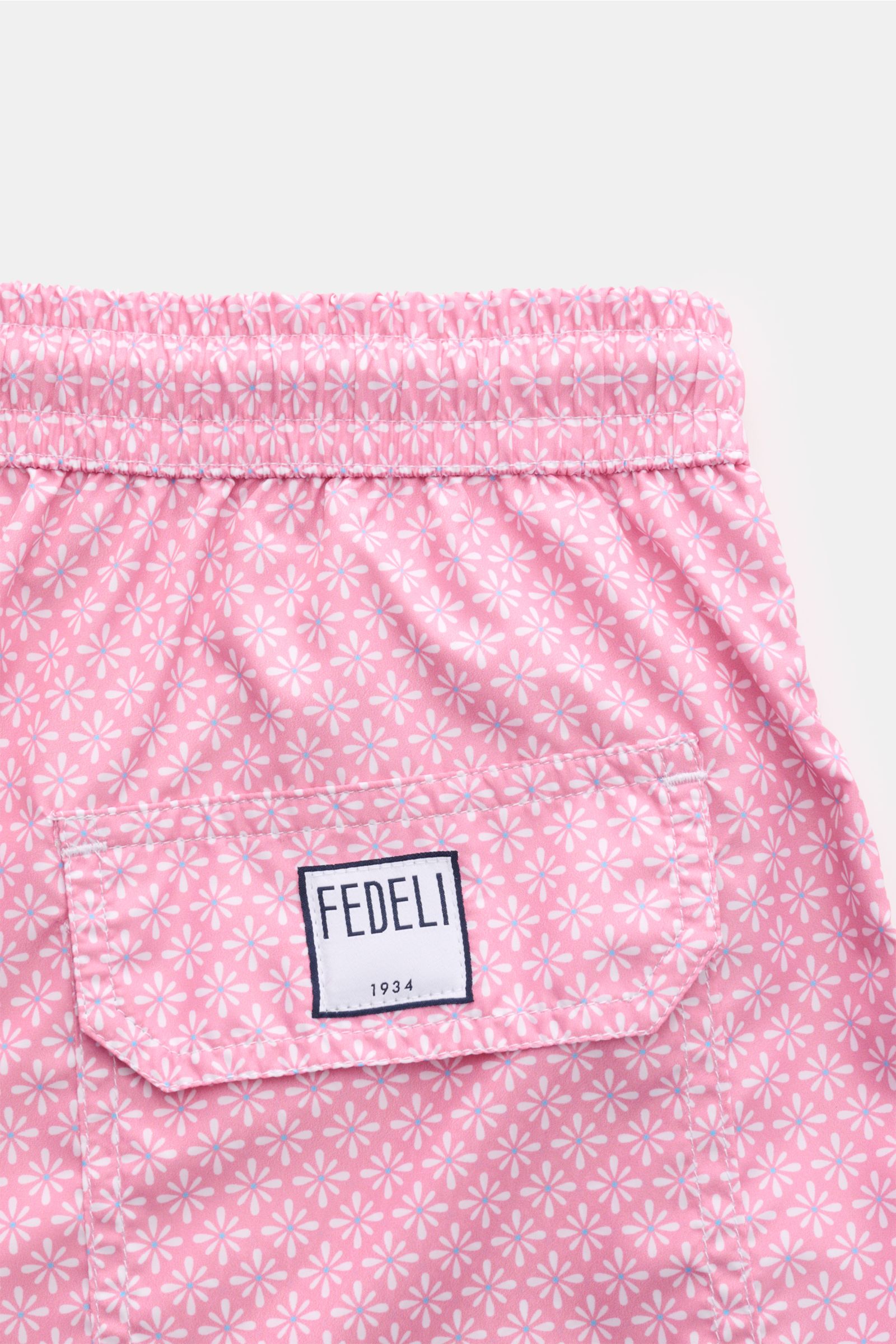 Close-up rear view of Fedeli Swim shorts 'Madeira Airstop' rose/white patterned with elastic waistband, side vents, back pocket with FEDELI label.

An essential for your summer vacation: These FEDELI swim shorts have an expressive pattern that adds sty