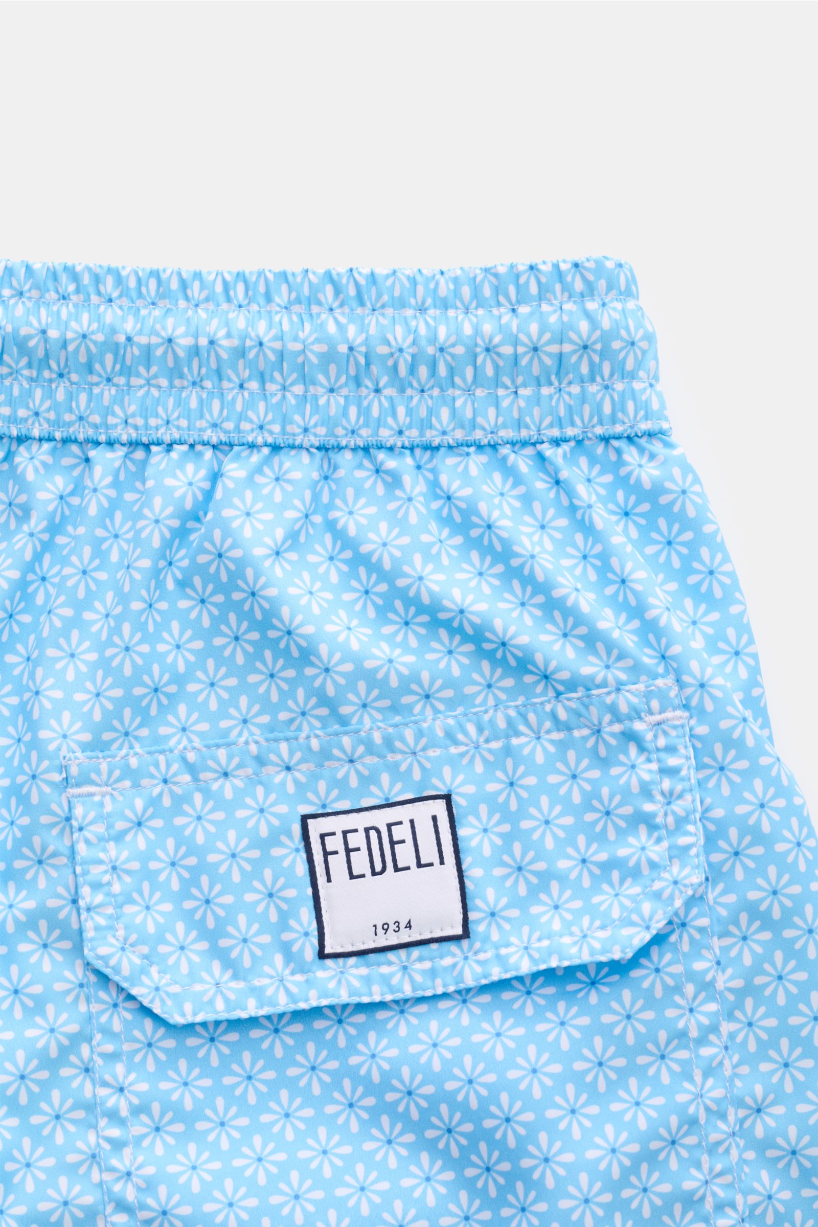 Close-up rear view of Fedeli Swim shorts 'Madeira Airstop' light blue/white patterned with elasticated waistband, back pocket, and FEDELI label.

Description: 
An essential for your summer vacation: These FEDELI swim shorts have an expressive pattern t