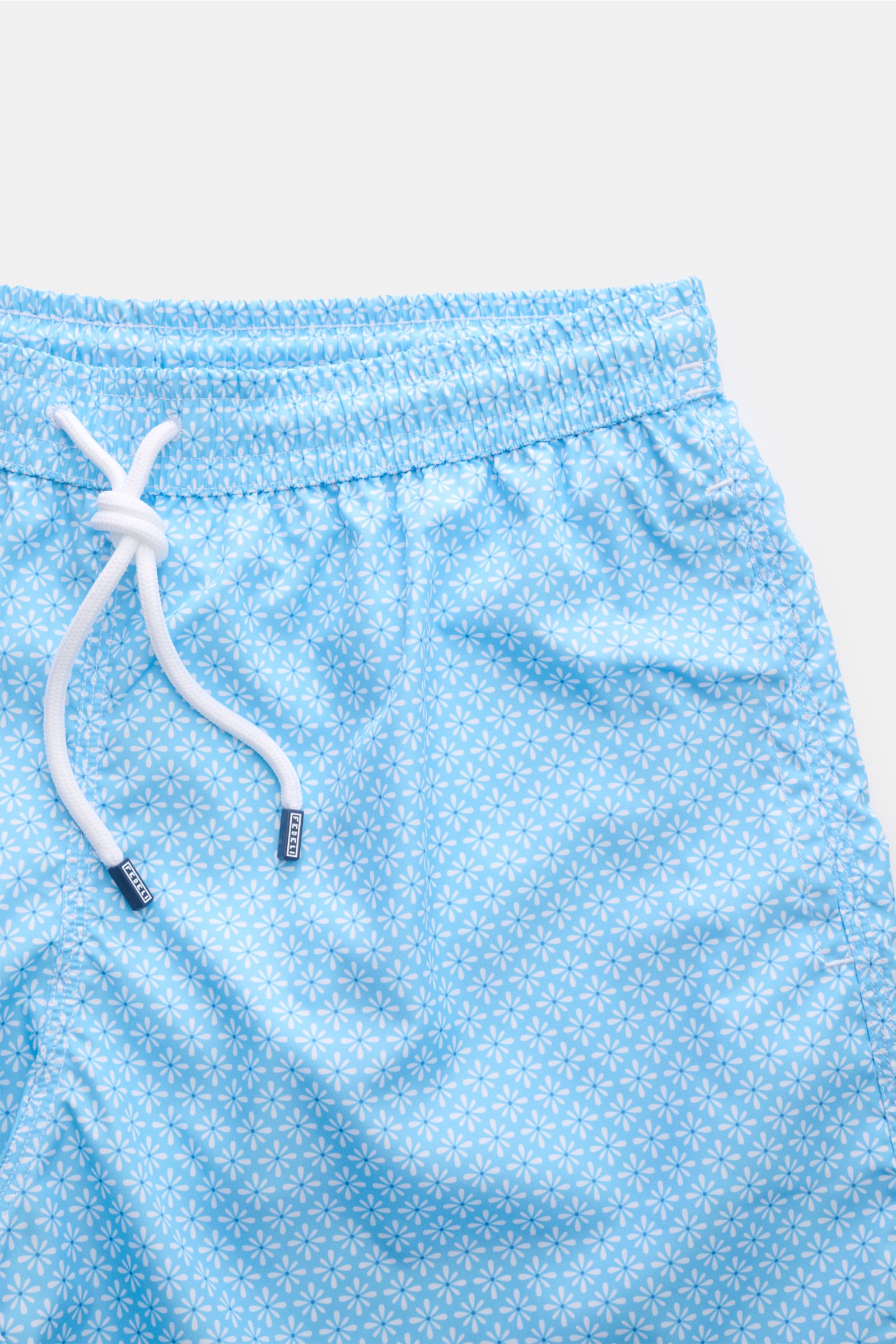 Close-up front view of Fedeli Swim shorts 'Madeira Airstop' light blue/white patterned with elasticated waistband and white drawstring.

Description: An essential for your summer vacation: These FEDELI swim shorts have an expressive pattern that adds s