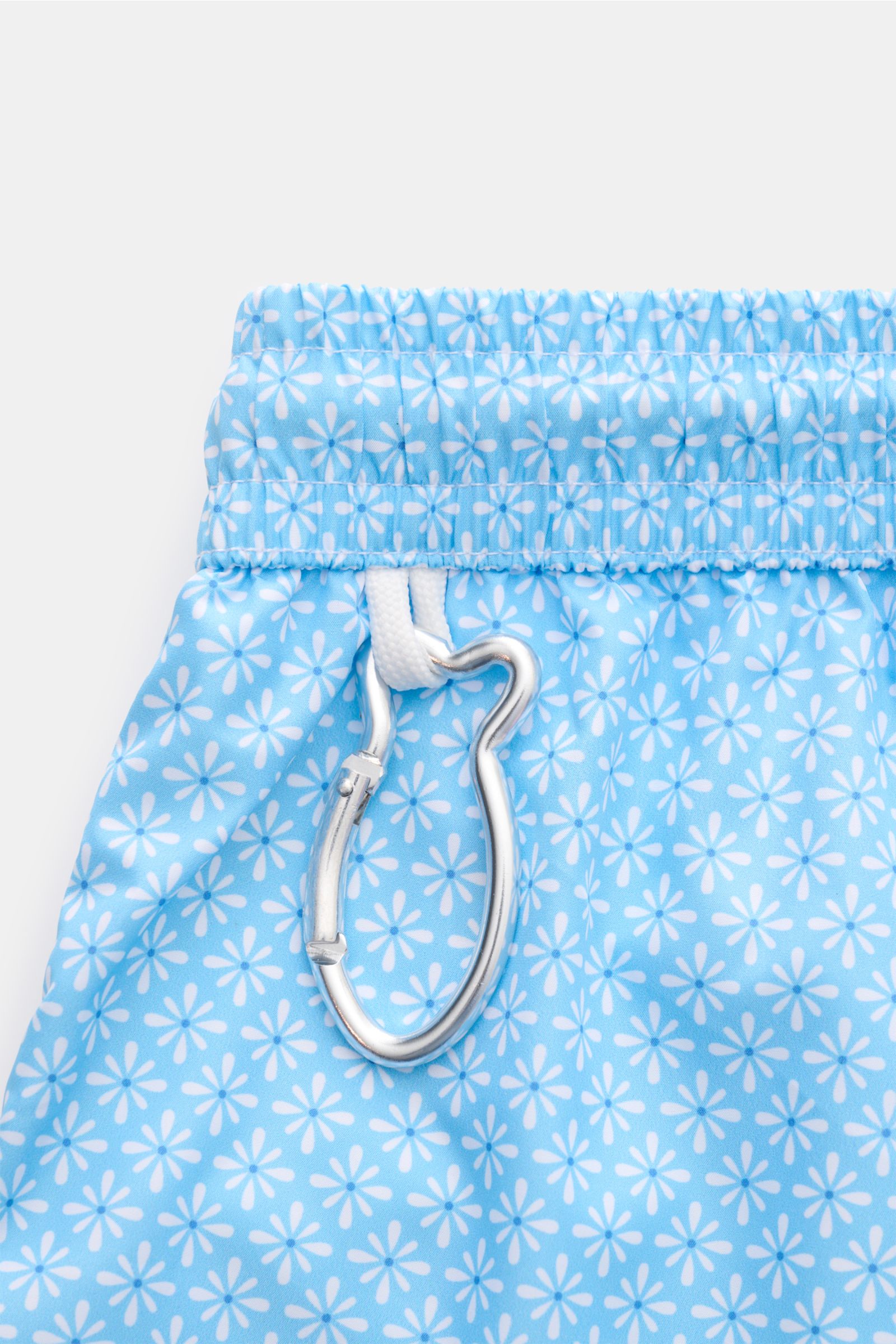 Close-up top view of Fedeli Swim shorts 'Madeira Airstop' light blue/white patterned with whale-shaped carabiner on elastic waistband.

Description:  
An essential for your summer vacation: These FEDELI swim shorts have an expressive pattern that adds 