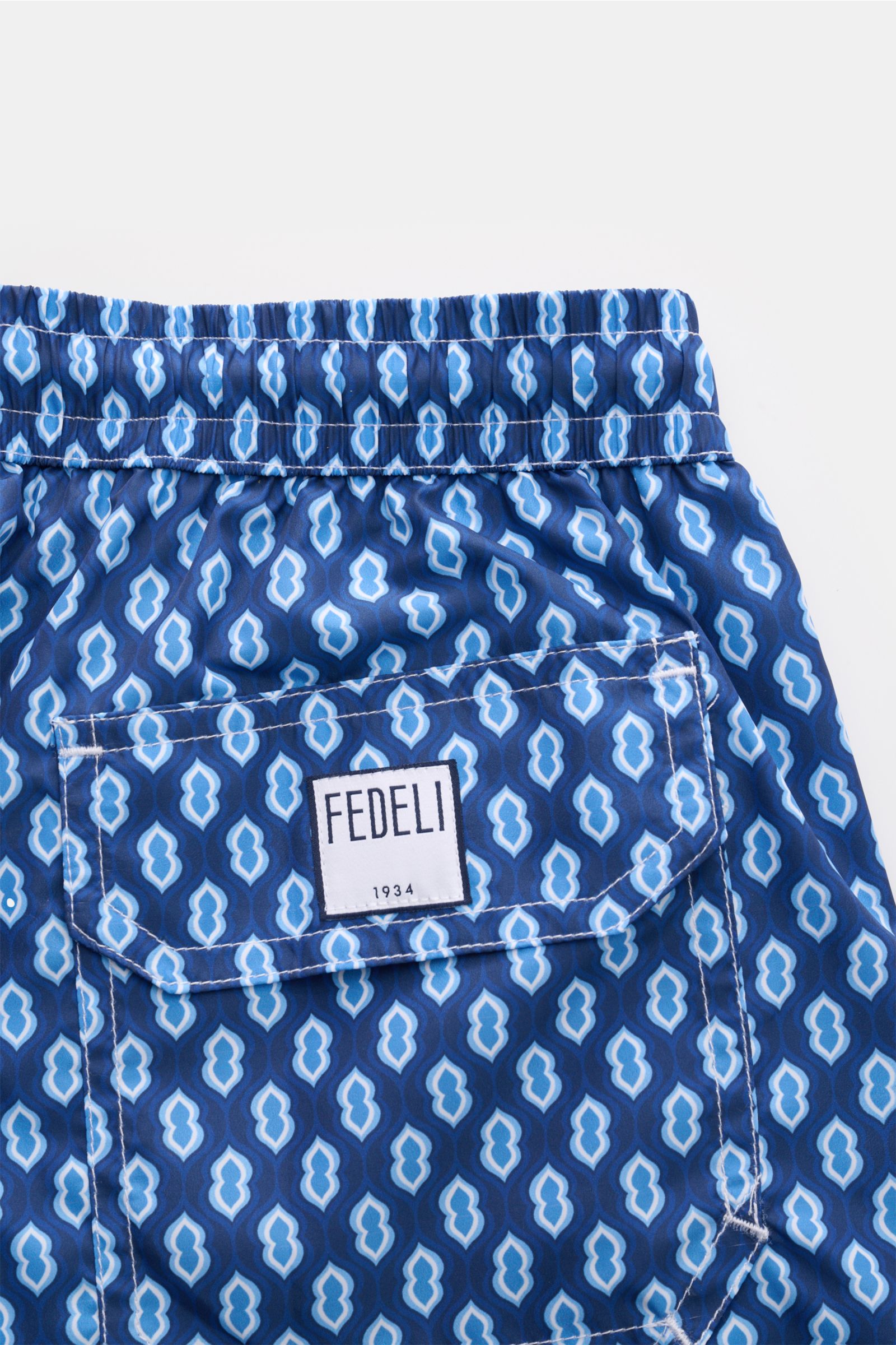 Close-up rear view of Fedeli Swim shorts 'Madeira Airstop' dark blue/blue/white patterned with elastic waistband and back pocket.

Description: An essential for your summer vacation: These FEDELI swim shorts have an expressive pattern that adds stylish