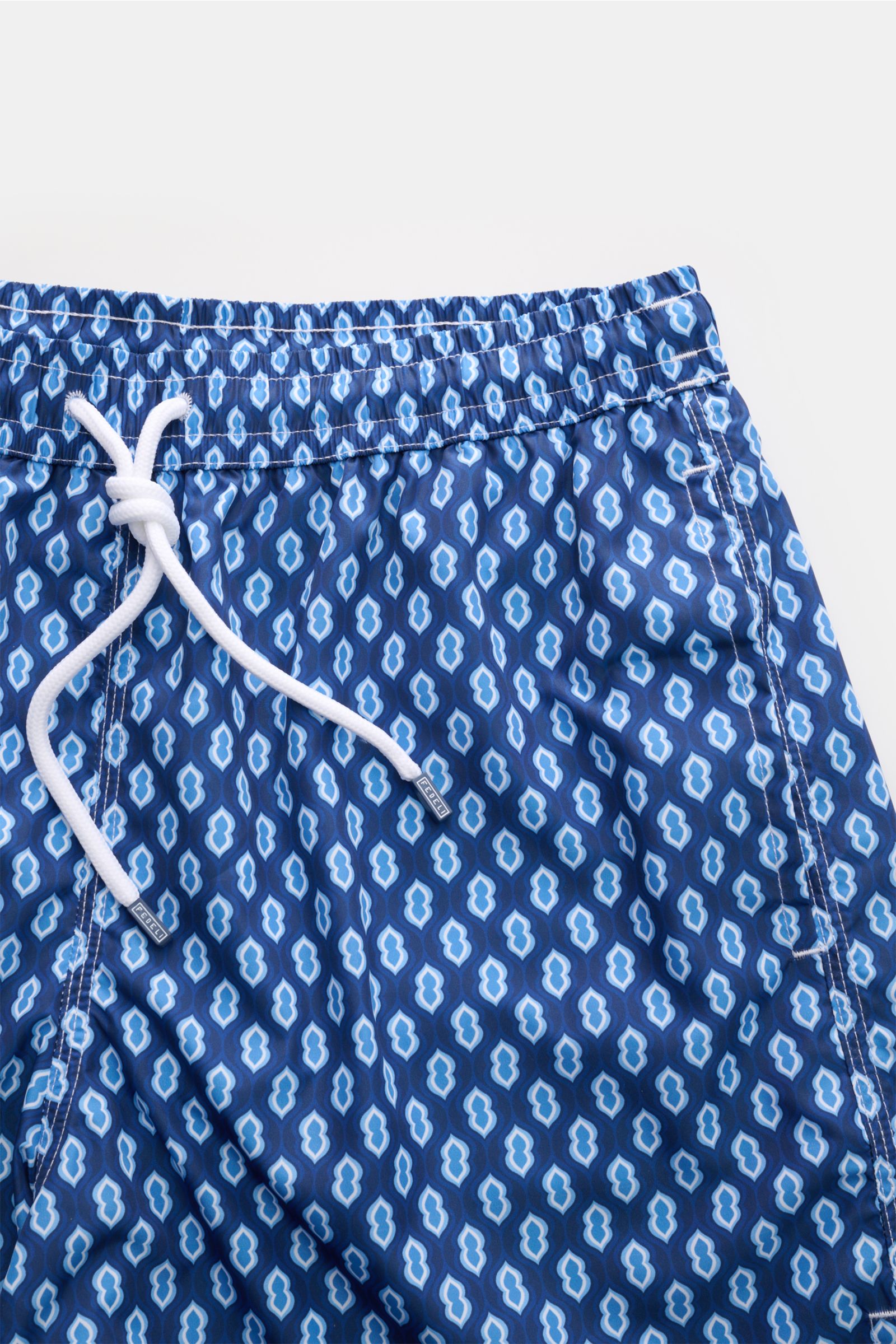 Close-up top-front view of Fedeli Swim shorts 'Madeira Airstop' dark blue/blue/white patterned with white drawstring and elasticated waistband.

An essential for your summer vacation: These FEDELI swim shorts have an expressive pattern that adds stylis