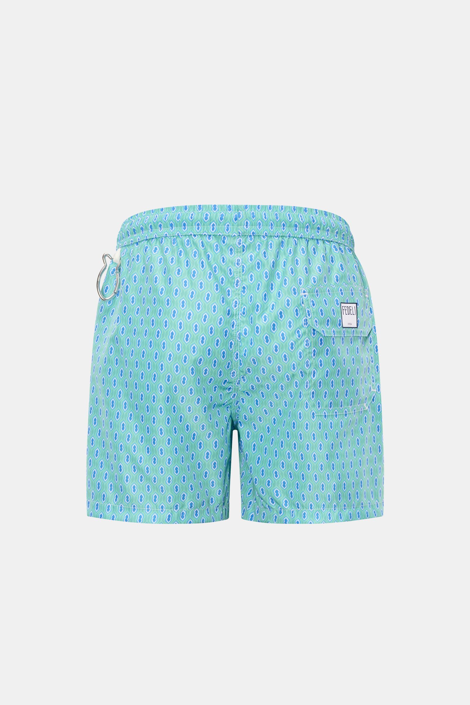 Rear view of Fedeli Swim shorts 'Madeira Airstop' turquoise/blue/white patterned with elastic waistband, back pocket, and whale-shaped carabiner.

An essential for your summer vacation: These FEDELI swim shorts have an expressive pattern that adds styl