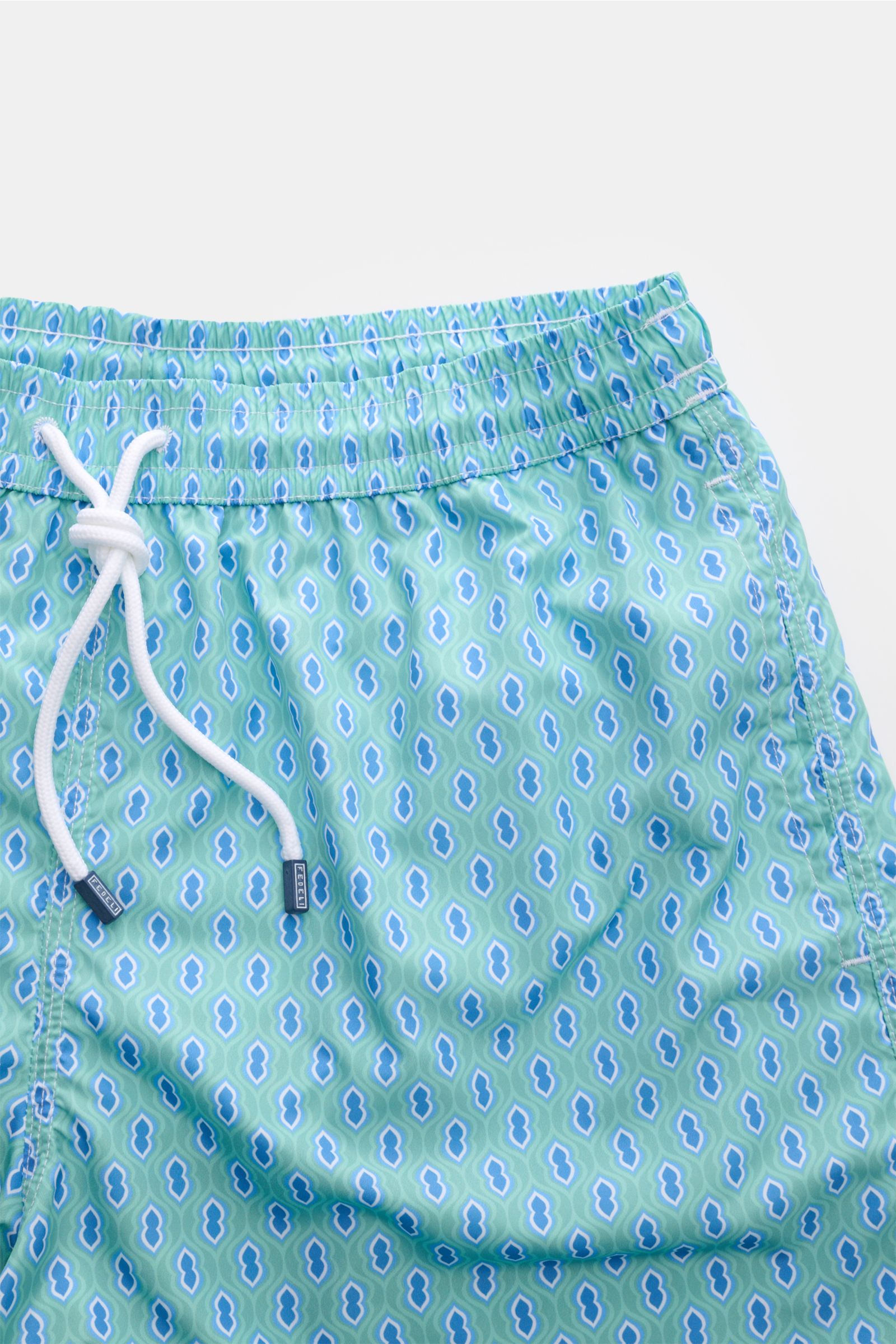 Fedeli Swim shorts 'Madeira Airstop' turquoise/blue/white patterned shown from a top front close-up, highlighting the elasticated waistband with white drawstring and graphic pattern. An essential for your summer vacation: These FEDELI swim shorts have an 