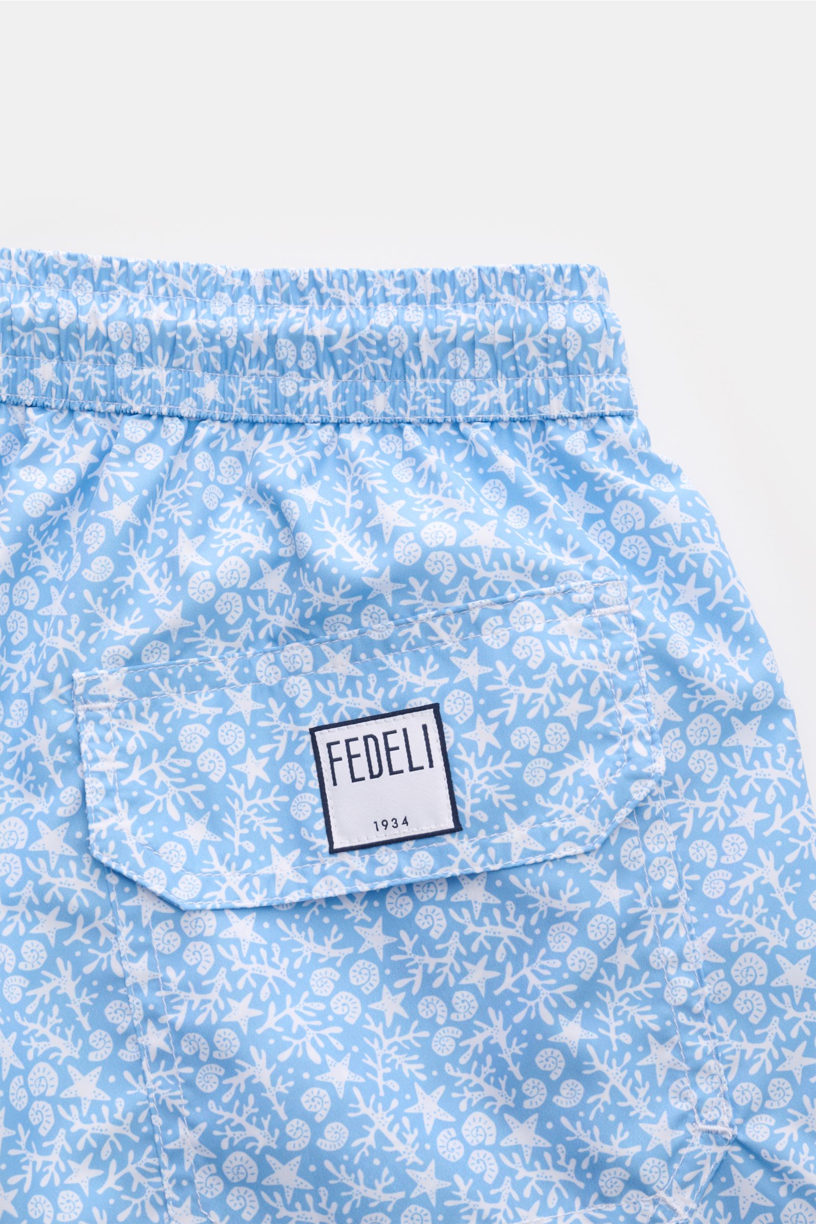 Close-up rear view of Fedeli Swim shorts 'Madeira Airstop' light blue/white patterned with elastic waistband, back pocket, and FEDELI label.

An essential for your summer vacation: These FEDELI swim shorts have an expressive pattern that adds stylish a