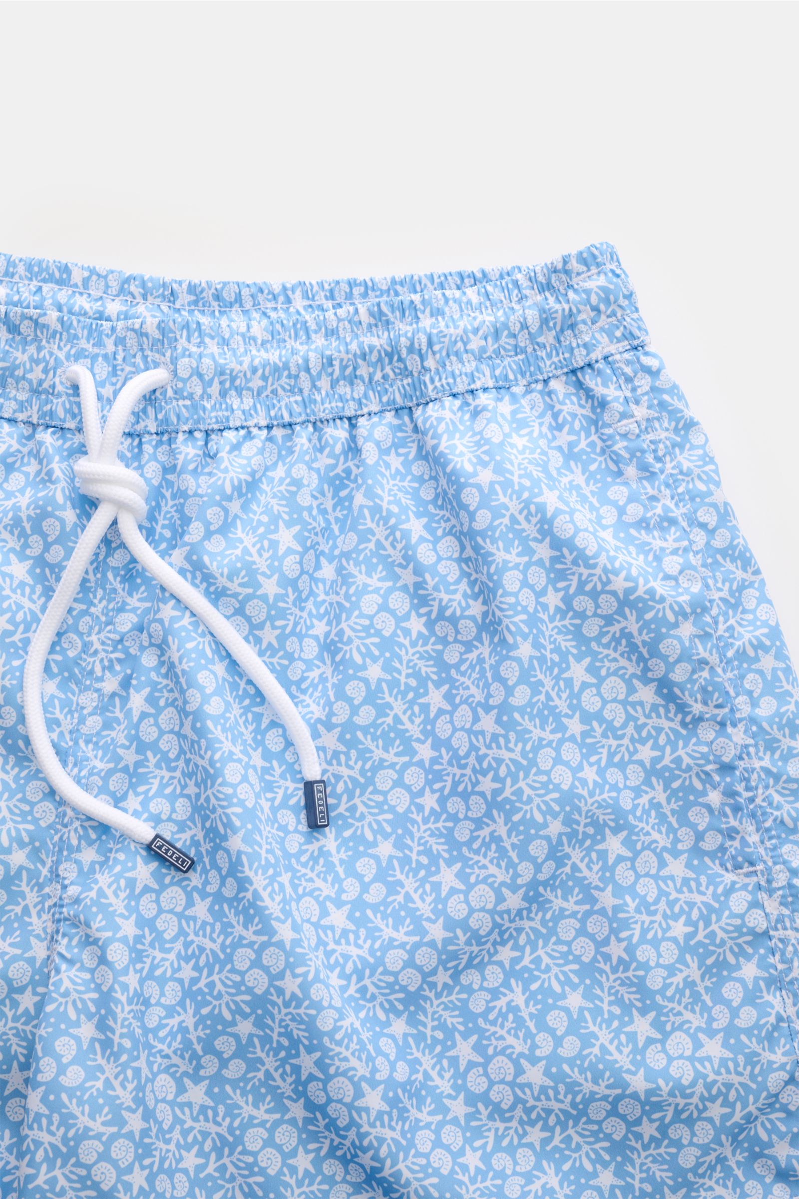 Close-up front view of Fedeli Swim shorts 'Madeira Airstop' light blue/white patterned with elastic waistband and white drawstring.

Description: An essential for your summer vacation: These FEDELI swim shorts have an expressive pattern that adds styli