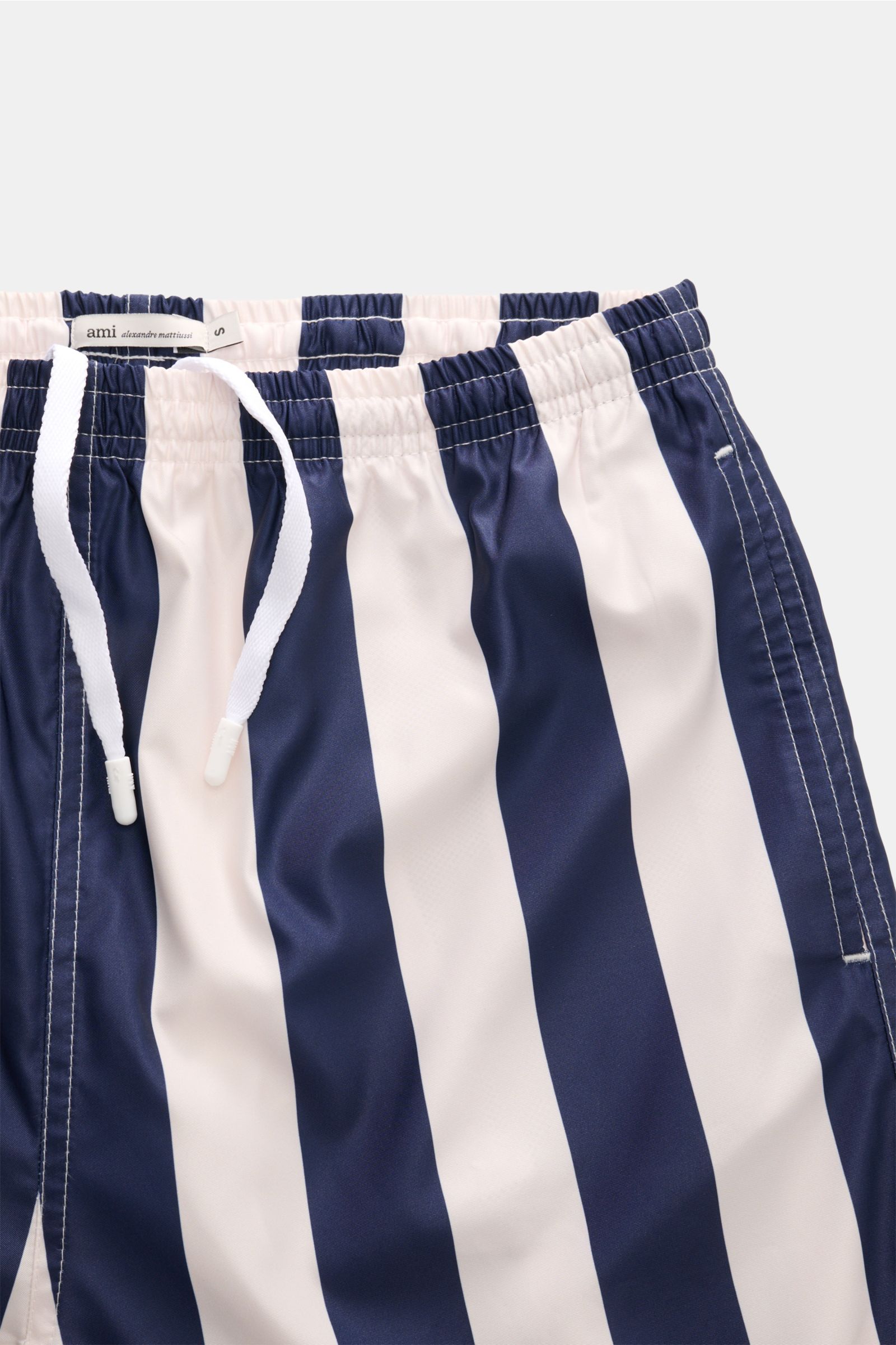 A close-up front view of Ami Paris Badeshorts navy/weiß gestreift showing the elastic waistband with white drawstring, made of high-quality microfiber with smooth touch, featuring regular fit, side seam pockets, back pocket with snap button, jersey lining