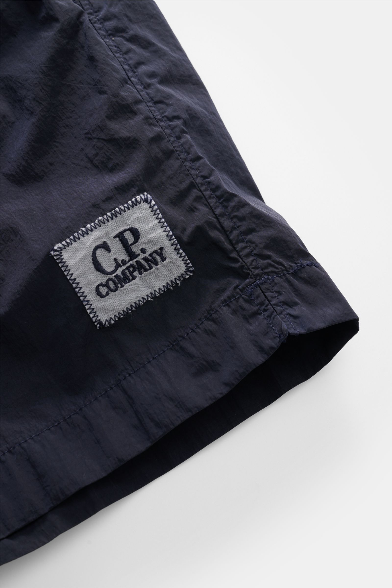 C.P. Company Badeshorts navy mit glänzender Oberfläche, Logo-Patch und glattem Griff, Nahaufnahme seitlich unten, Regular Fit, elastischer Bund.
