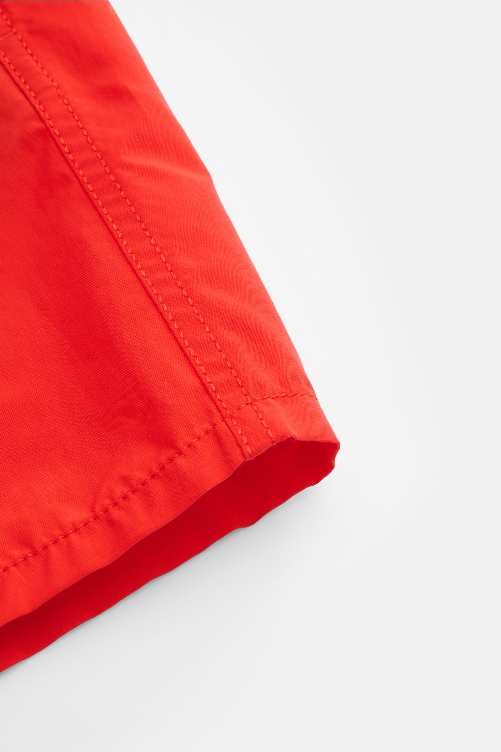 Nahaufnahme der roten Vilebrequin Badeshorts 'Moorea' aus hochwertiger Microfaser, seitliche Naht und leichter Griff, fotografiert aus seitlicher Perspektive.