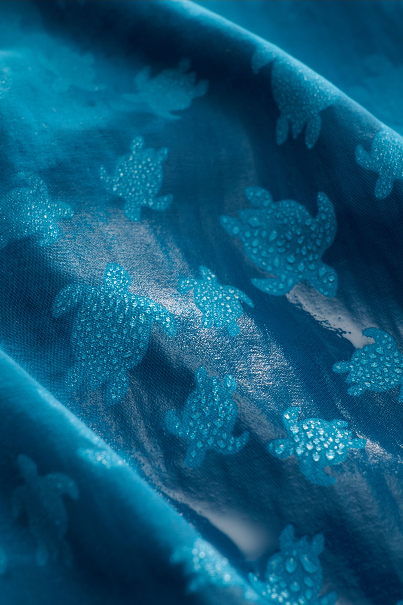 Nahaufnahme der wasserreaktiven Microfaser der Vilebrequin Badeshorts 'Moorea Magic' petrol mit Muster, Blick auf Stoffdetails.