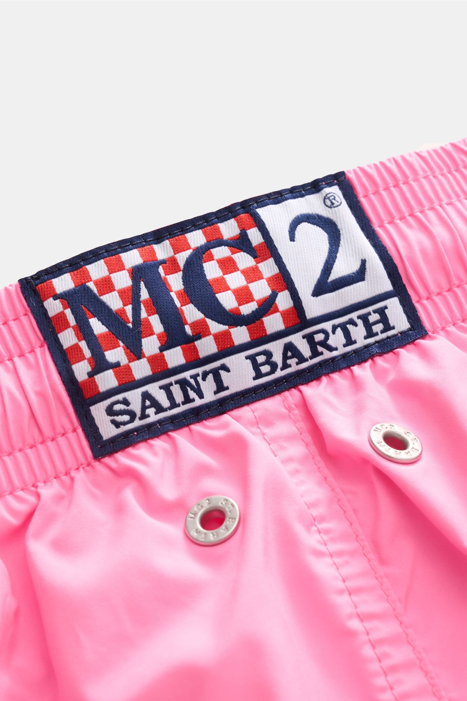 Nahaufnahme der pinkfarbenen MC2 Saint Barth Badeshorts 'Lightning Pantone' aus recycelter Microfaser, Fokus auf elastischen Bund mit Kordelzug, Metallösen und Markenlabel. Fotografiert aus schräger Draufsicht.